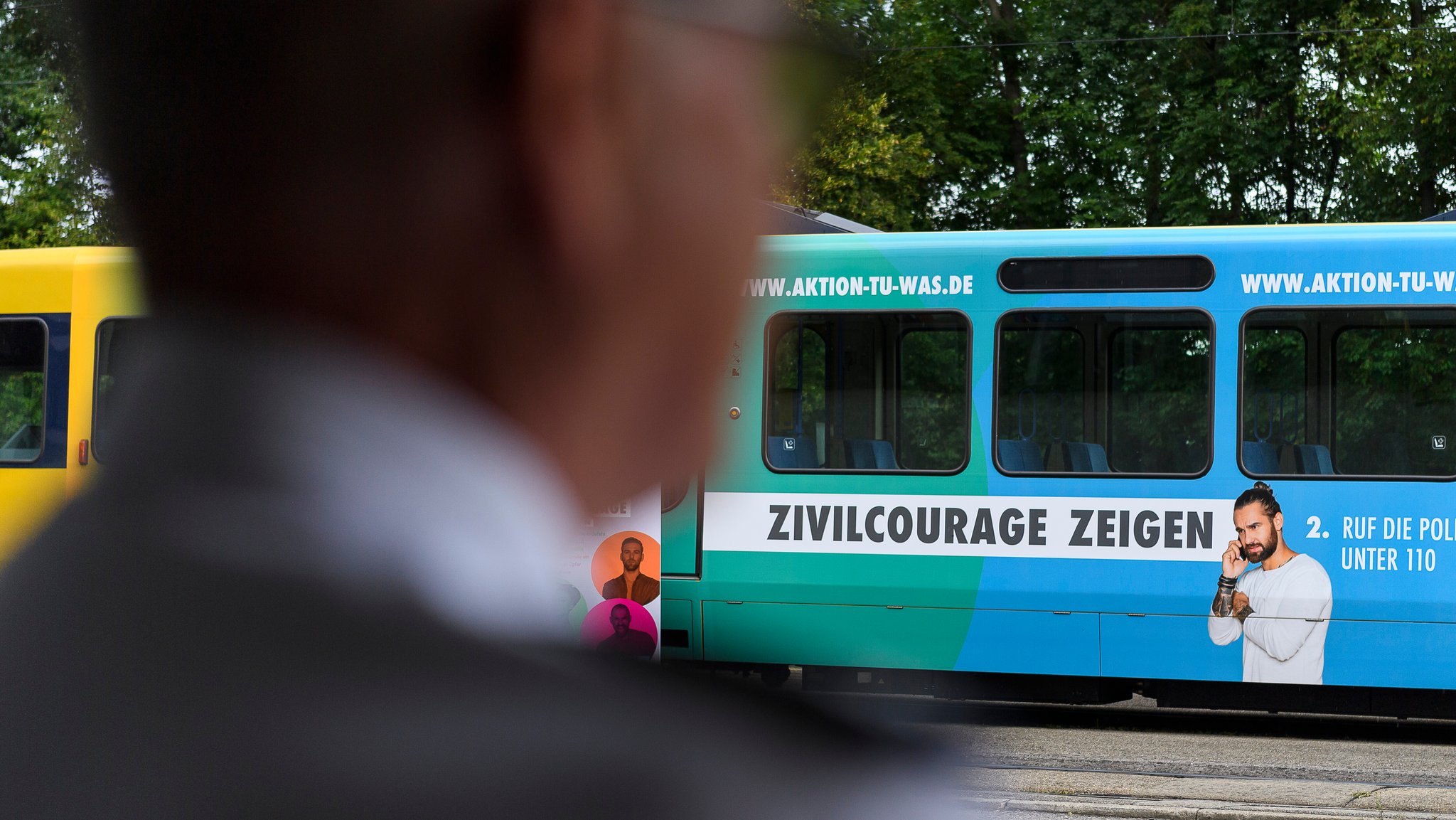 Ein Polizist, unscharf im Vordergrund,  schaut auf die mit Werbung beklebte Straßenbahn