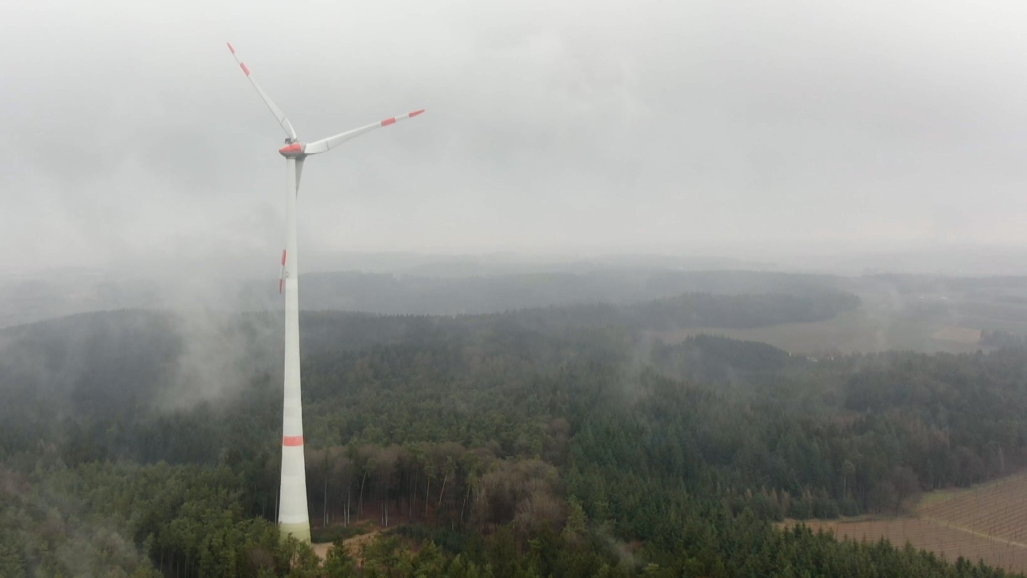 Ein wolkenumhangenes Windrad in einer waldigen Umgebung. Es steht in der Nähe von Pfaffenhofen und soll dauerhaft für sichere Energie sorgen.