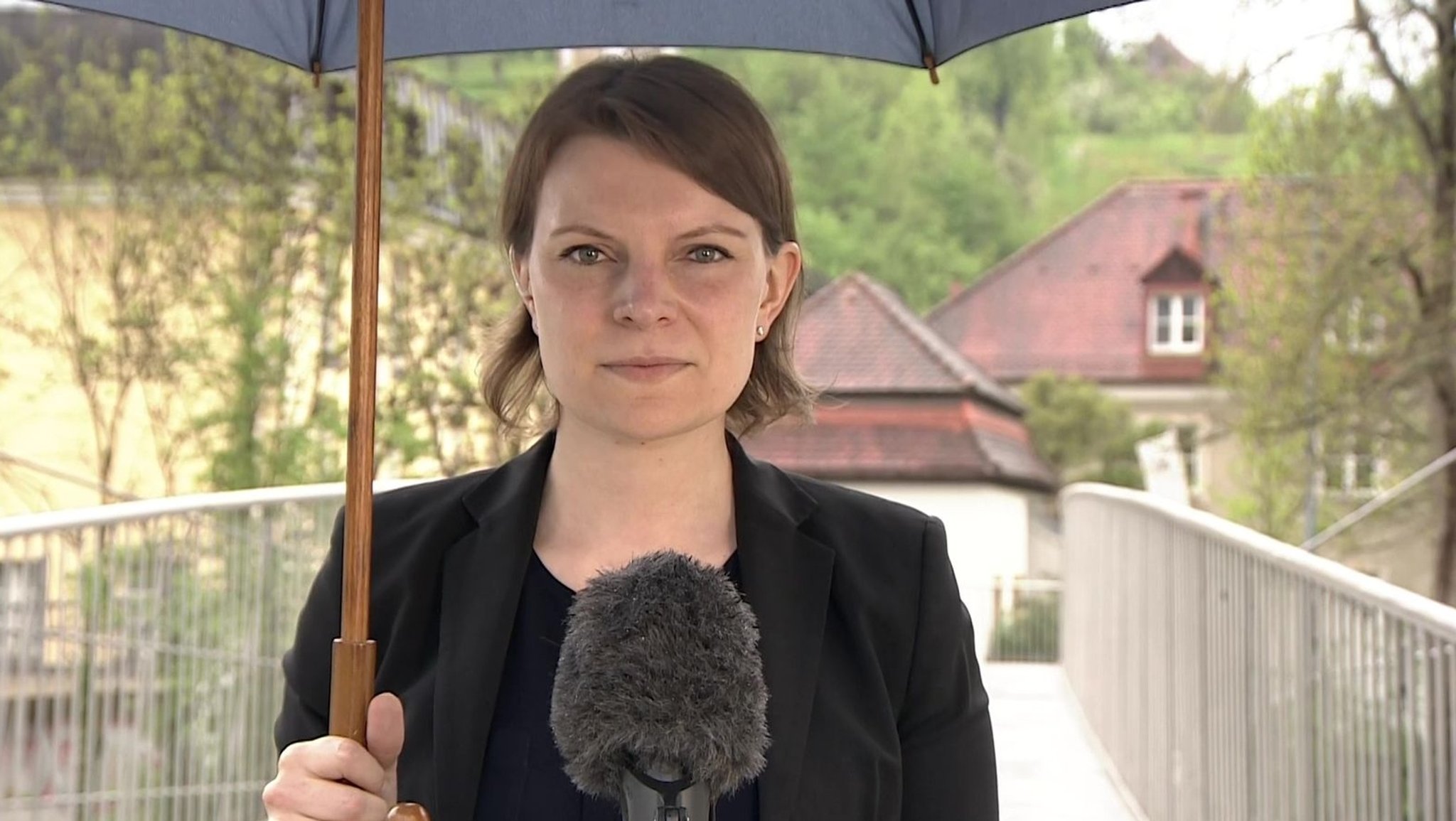 Emmi Zeulner steht mit Regenschirm auf einer Brücke vor einem Mikrofon.