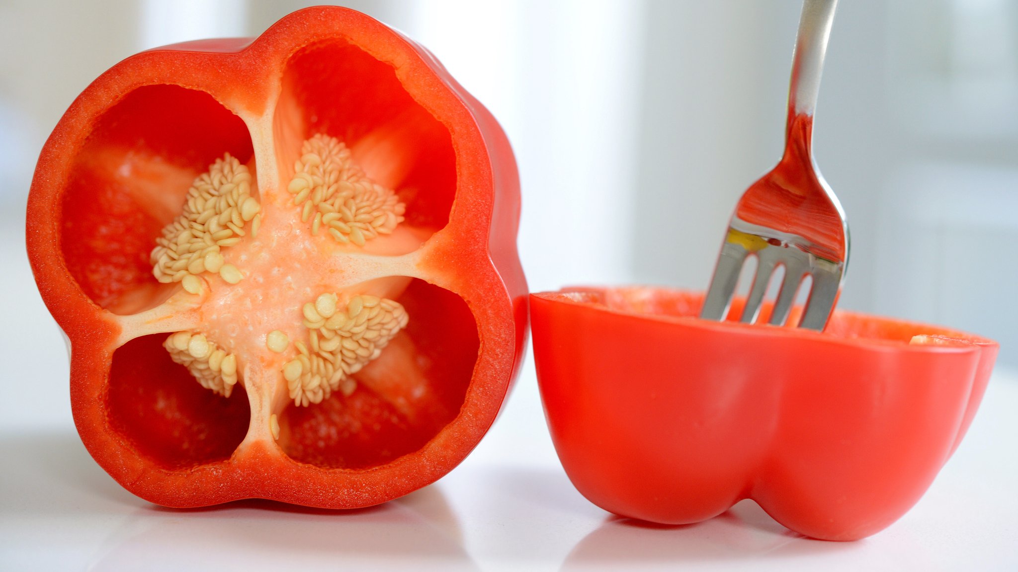 Halbierte Paprika mit Kernen. In einer Hälfte steckt eine Gabel
