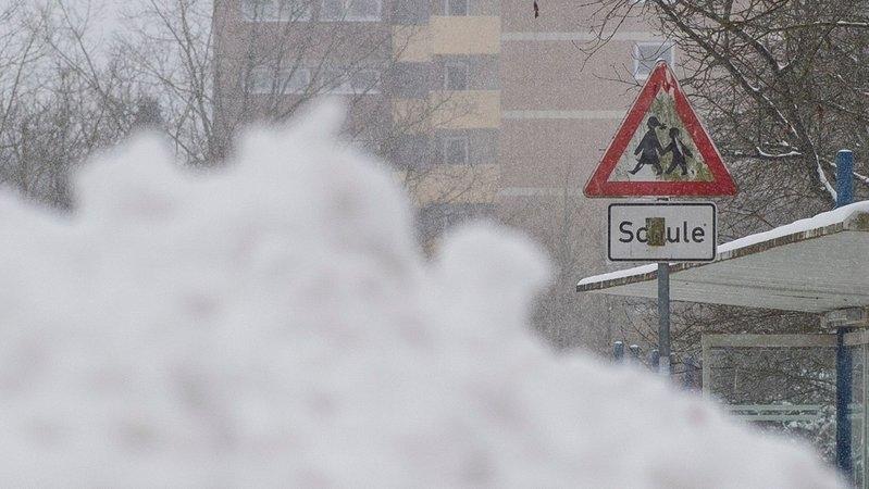 Ein Schneeberg  vor einer Schule, daneben ein Verkehrszeichen mit der Aufschrift "Schule". 