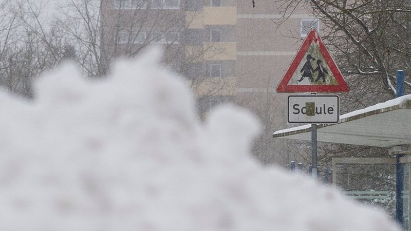 Ein Schneeberg  vor einer Schule, daneben ein Verkehrszeichen mit der Aufschrift "Schule". 