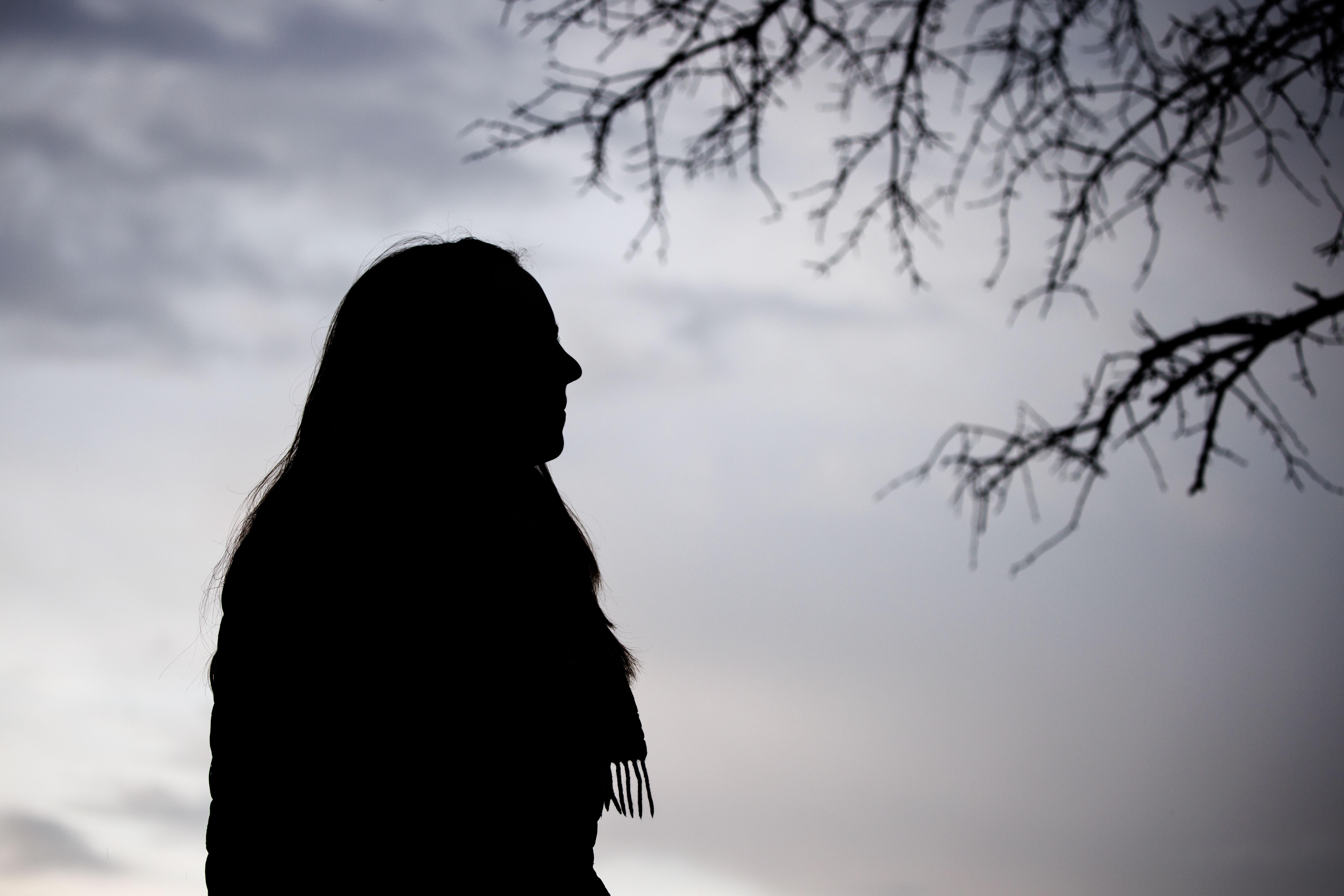 Eine Frau steht bei trübem Wetter unter einem kahlen Baum.