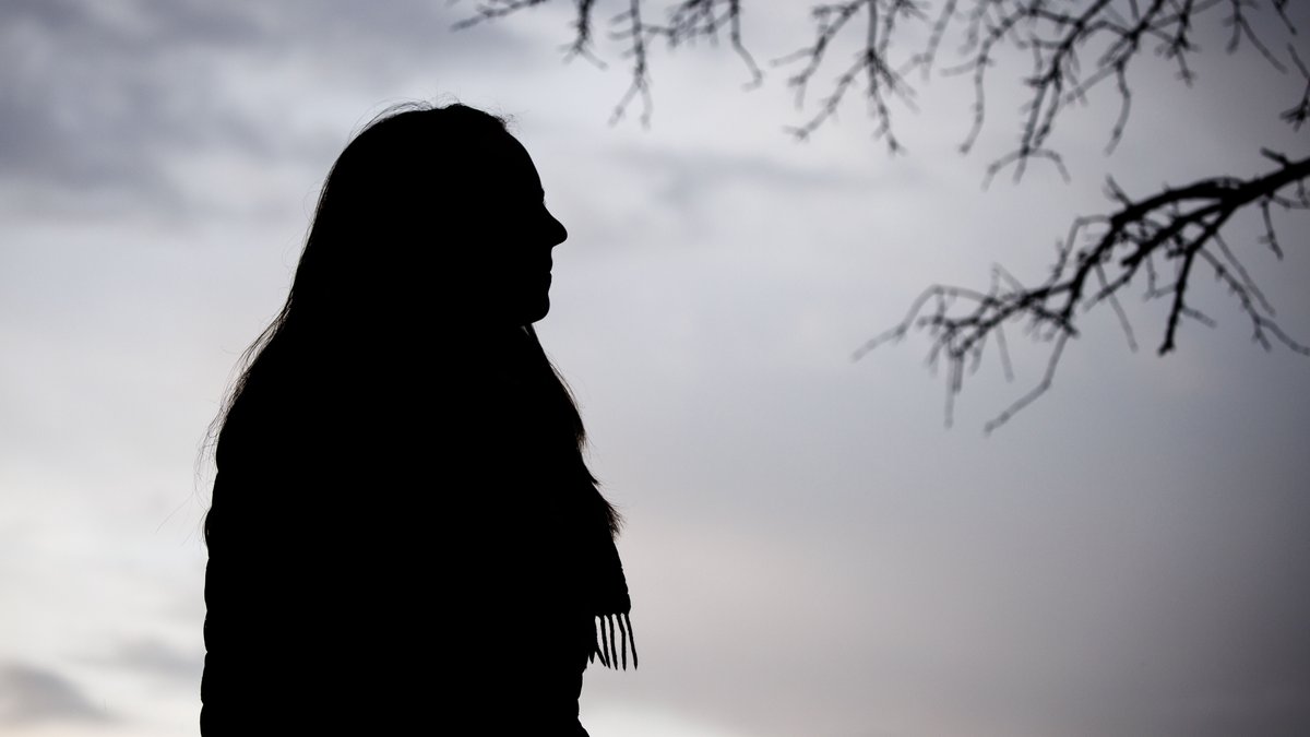 Eine Frau steht bei trübem Wetter unter einem kahlen Baum.