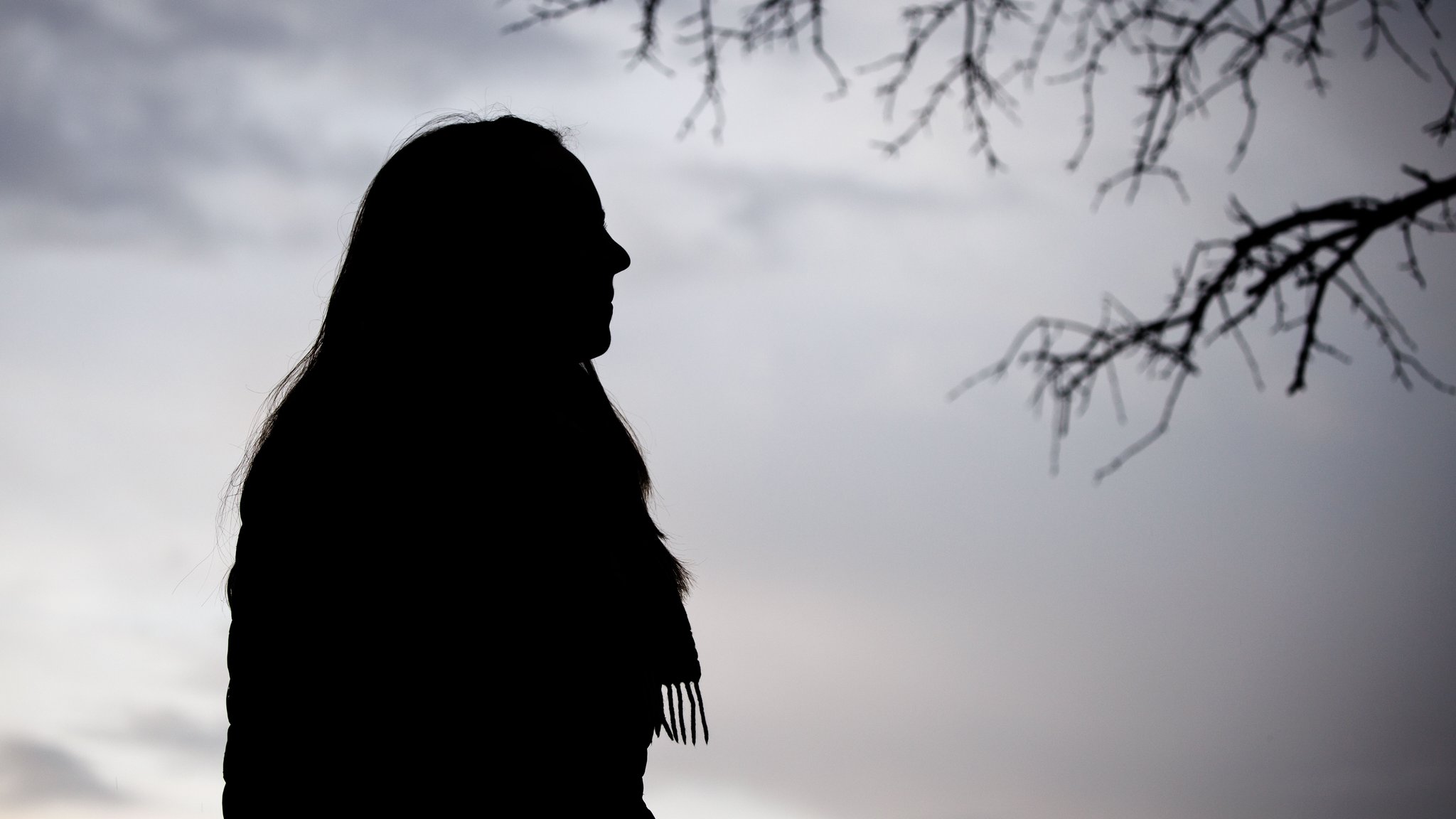Eine Frau steht bei trübem Wetter unter einem kahlen Baum.