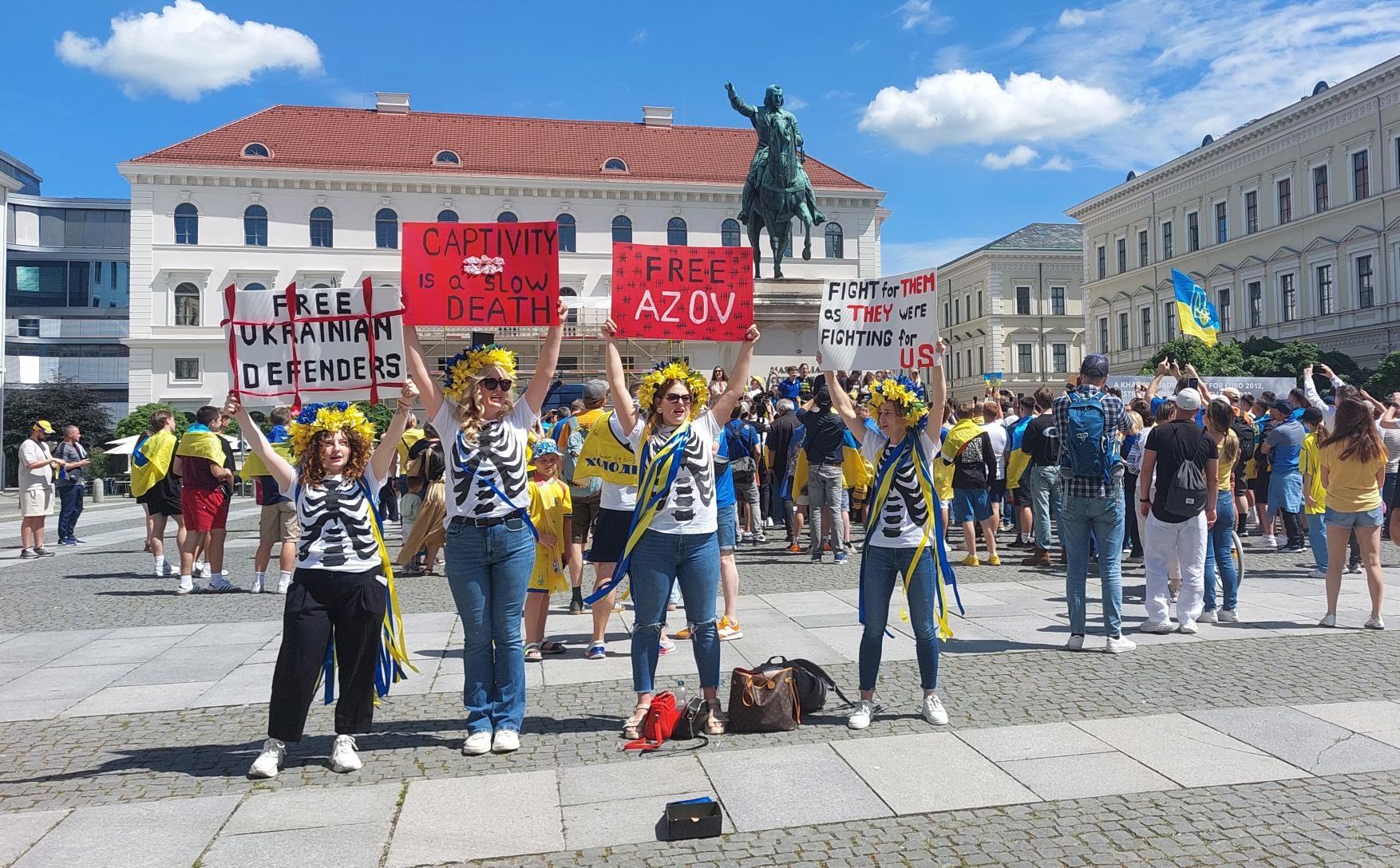 Vier Frauen in ukrainischen Farben halten Schilder in die Höhe, auf einem steht: "Fight for them as they were fighting for us."