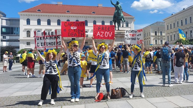 Vier Frauen in ukrainischen Farben halten Schilder in die Höhe, auf einem steht: "Fight for them as they were fighting for us."