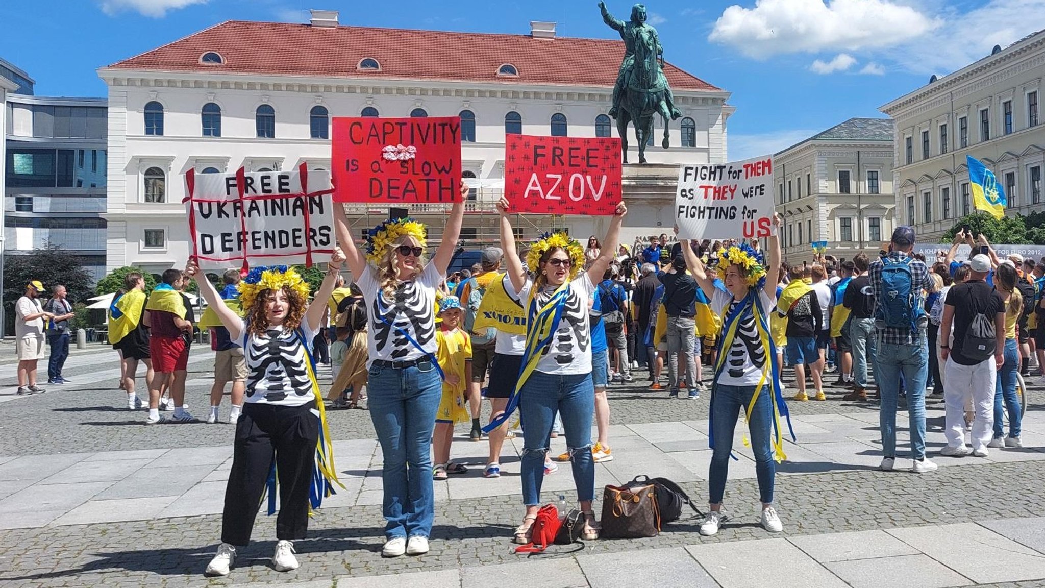 Vier Frauen in ukrainischen Farben halten Schilder in die Höhe, auf einem steht: "Fight for them as they were fighting for us."