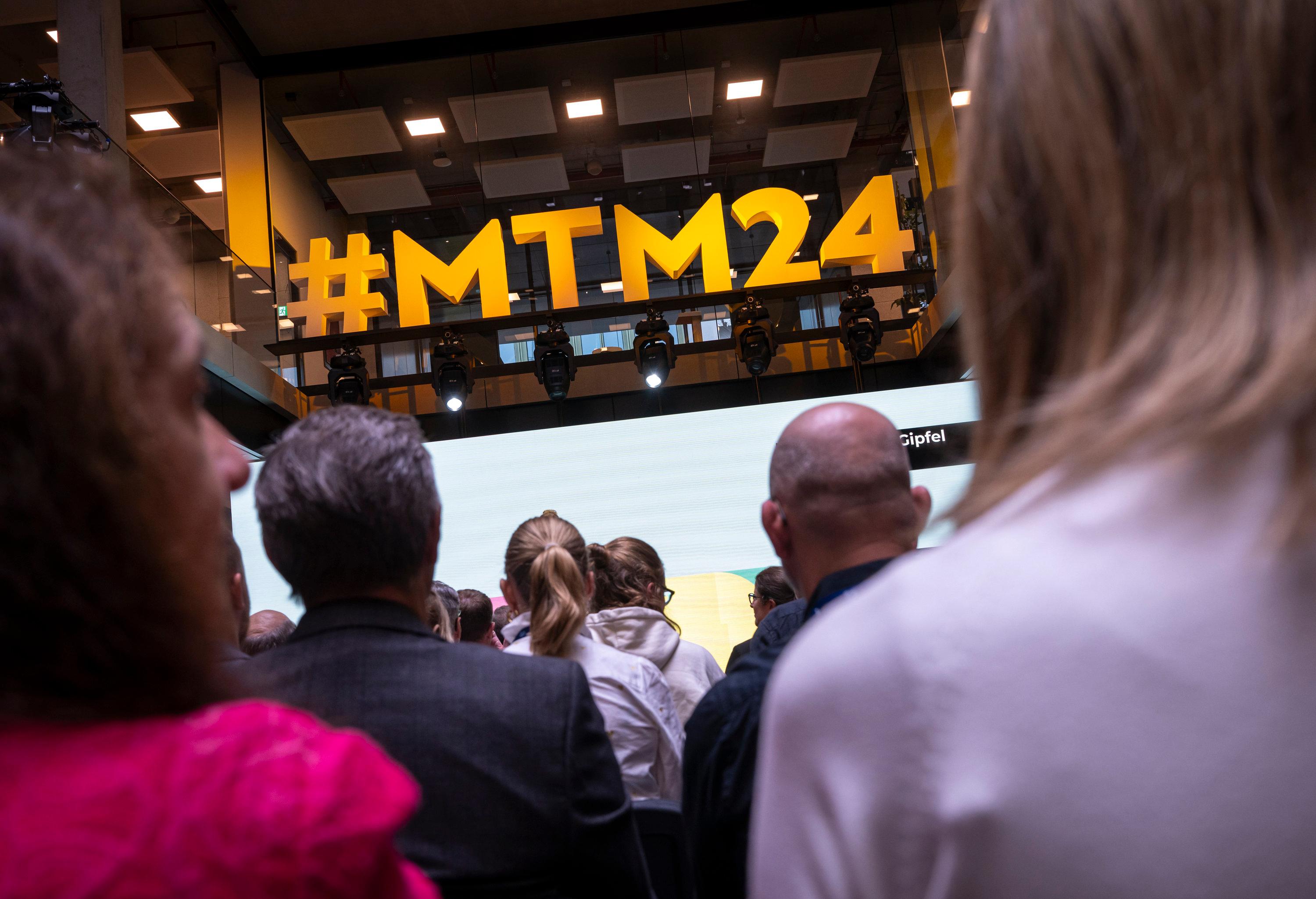 Der Hashtag #MTM24 ist bei den 38. Medientage München über den Köpfen der Teilnehmer zu sehen
