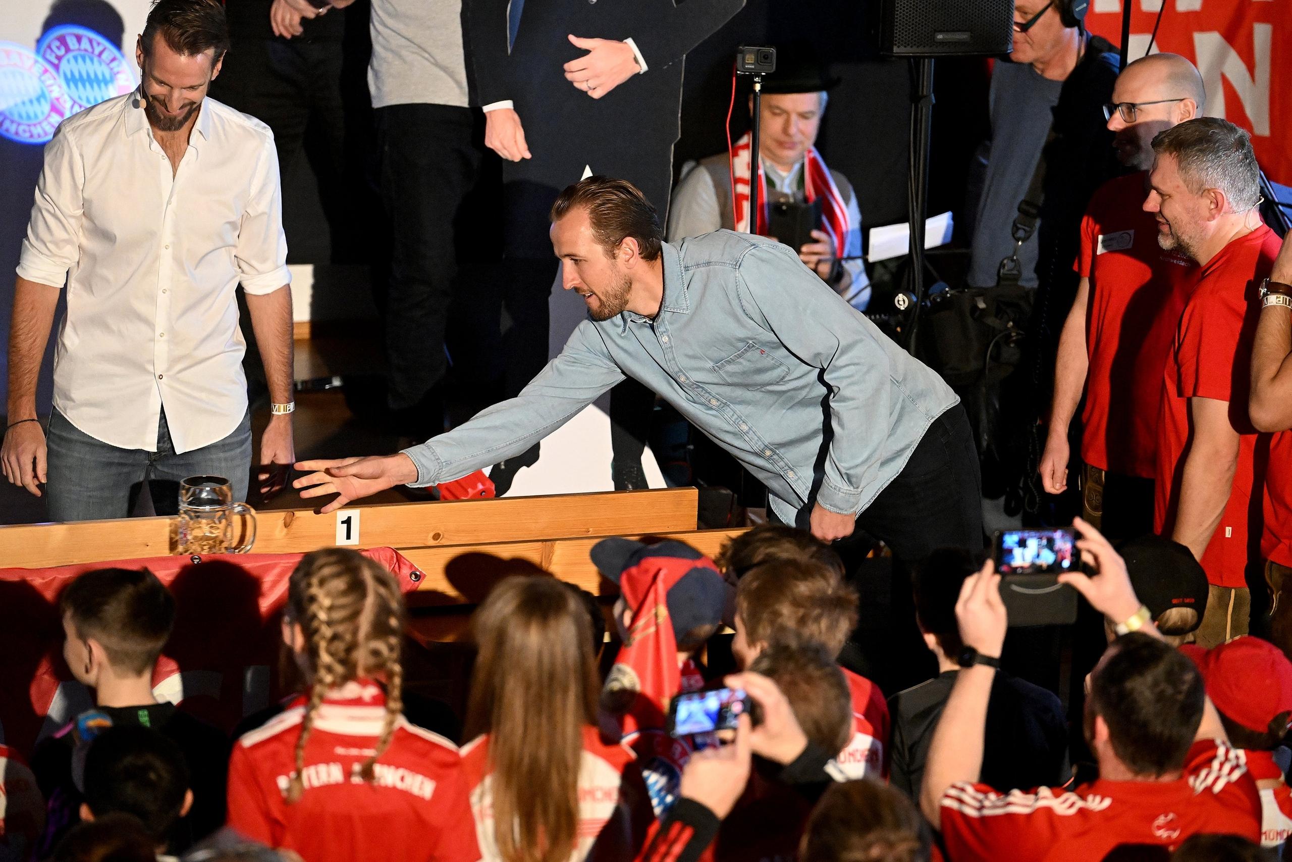 28.01.2024, Bayern, Kirchweidach: Fußball: Bundesliga, FC Bayern München. FC-Bayern-Spieler Harry Kane aus England schiebt einen Maßkrug beim Maßkrug-schieben im Fanclub «Die Roten» in Kirchweidach. Er erhielt dort eine Trophäe für seinen Sieg bei einer bayerischen Miniolympiade in Form einer Torjägerkanone, mit der er auch Schnupftabak genießen könnte. Die Stars des FC Bayern holten ihre wegen des Winterwetters im Dezember verschobenen Fanclubbesuche nach. 