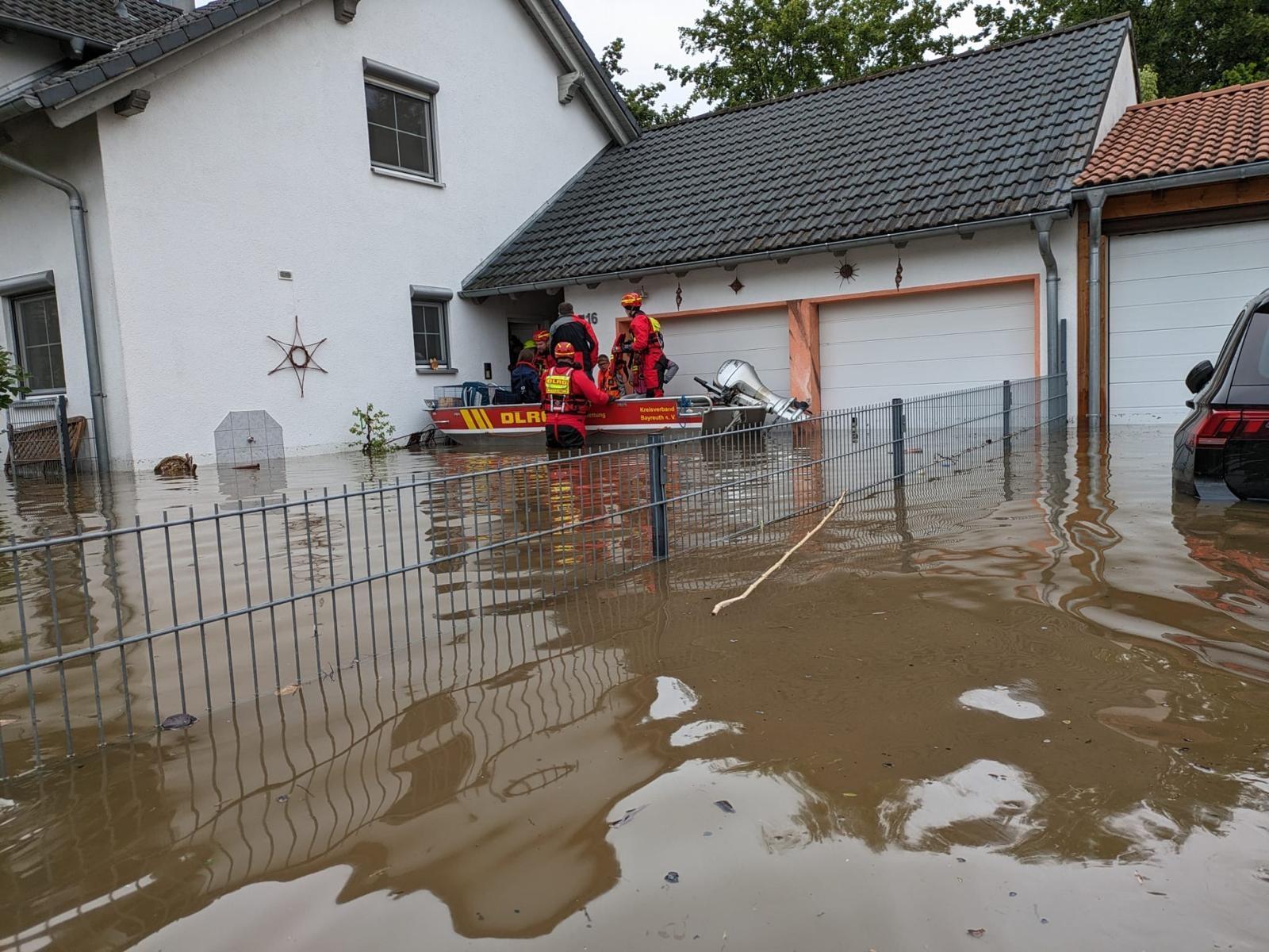 Einsatzkräfte der DLRG Oberfranken steht an einem überschwemmten Haus. 