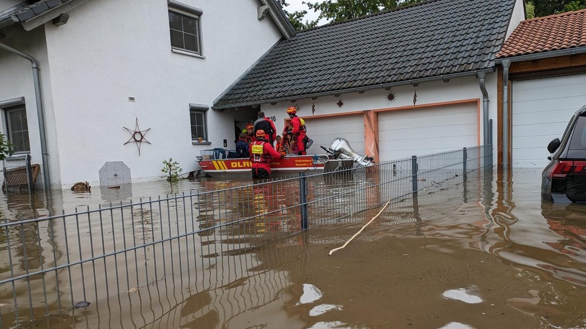 Einsatzkräfte der DLRG Oberfranken steht an einem überschwemmten Haus. 
