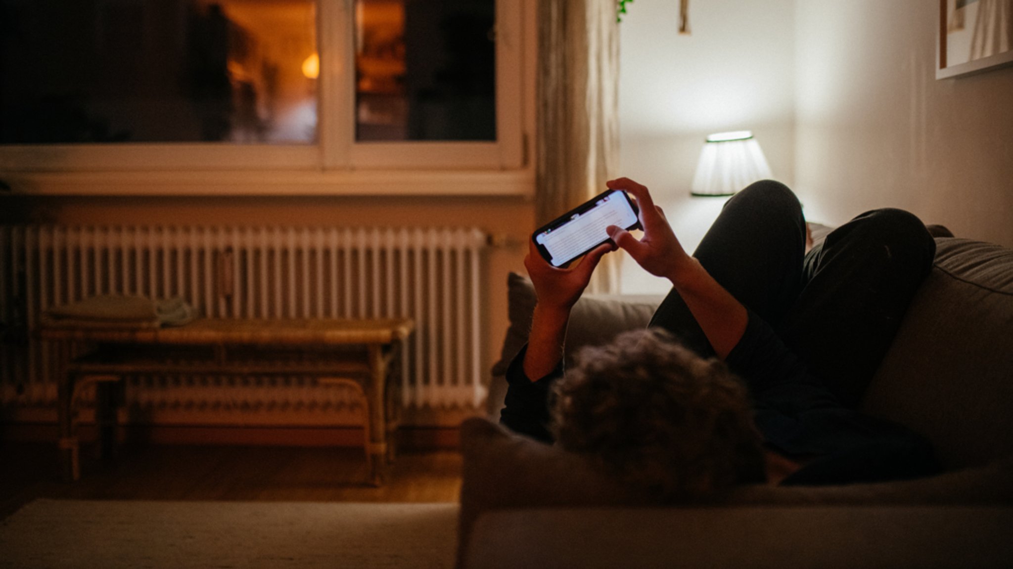 Ein junger Mann liegt auf dem Sofa und schaut in sein Smartphone