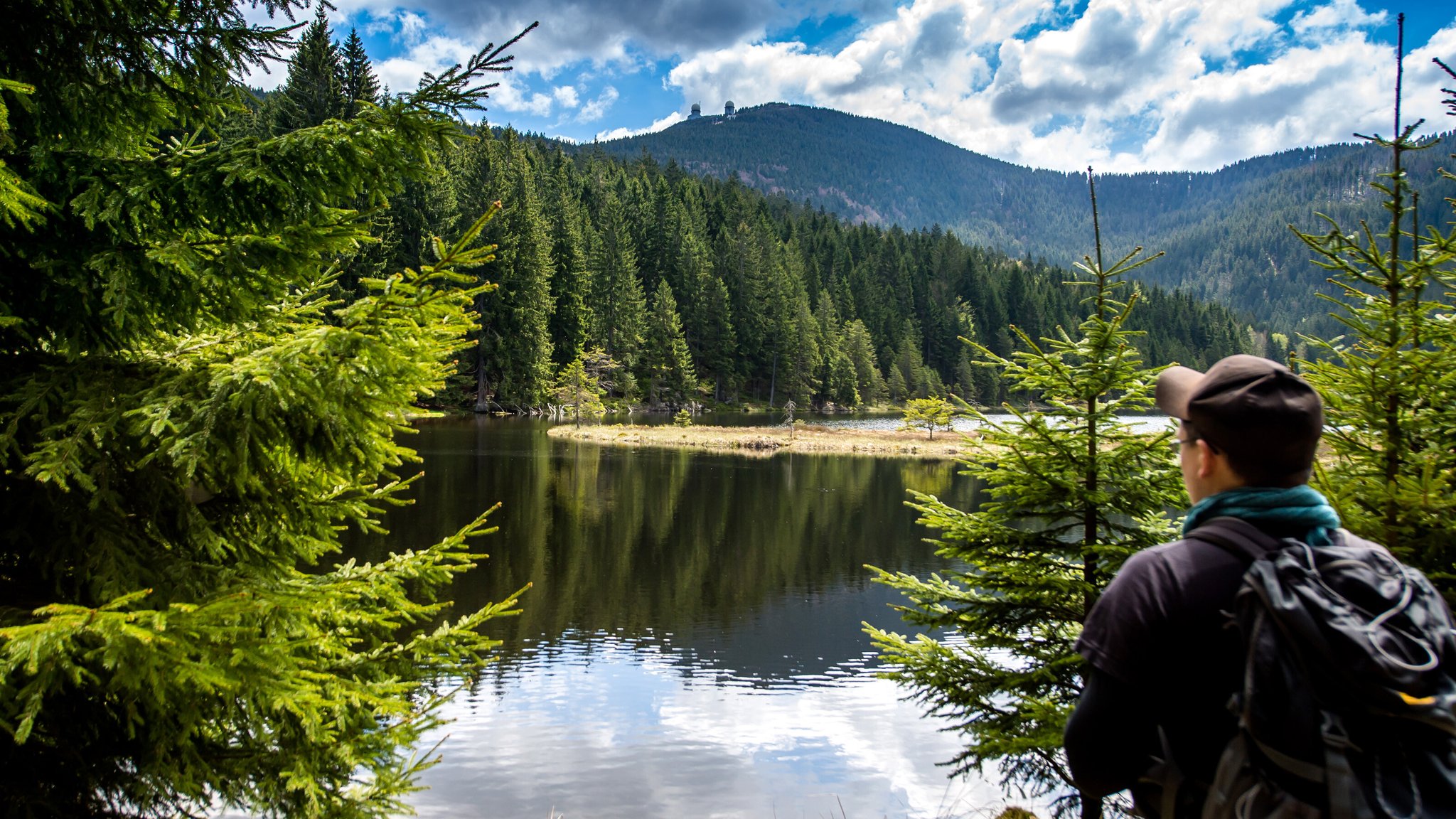 Wanderer laufen im bayerischen Wald am kleinen Arbersee vorbei, im Hintergrund ist der Gipfel des Großen Arbers zu sehen.