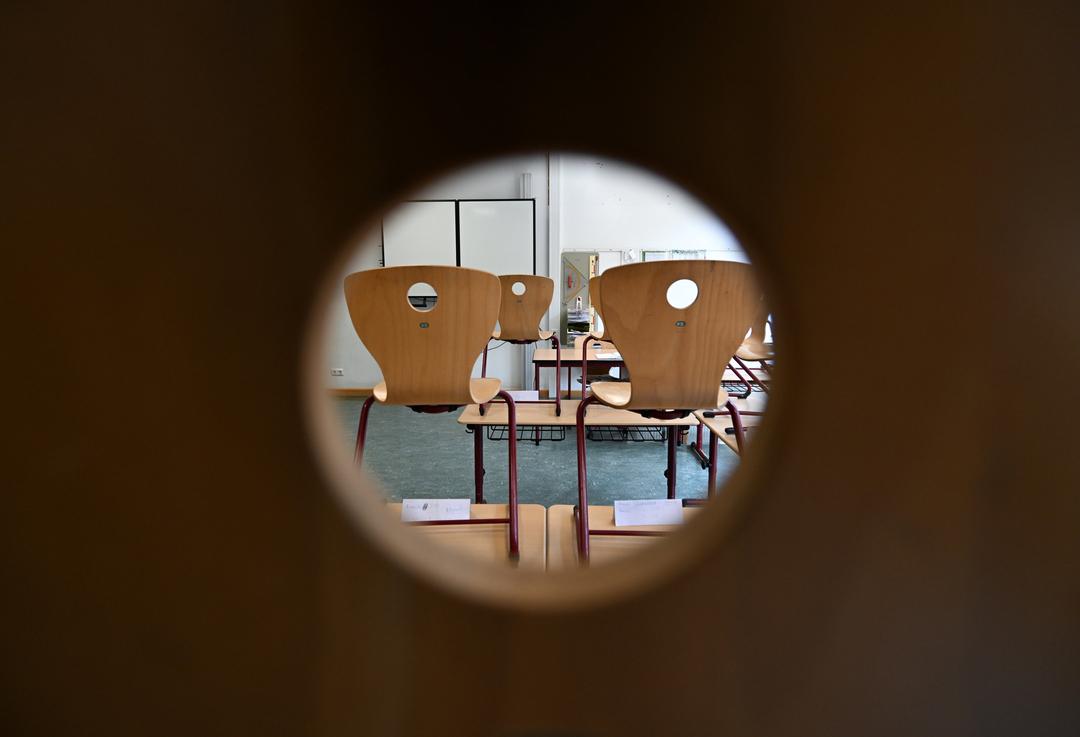 Blick durch ein Türloch in ein Klassenzimmer, in dem die Stühle auf den Bänken stehen.