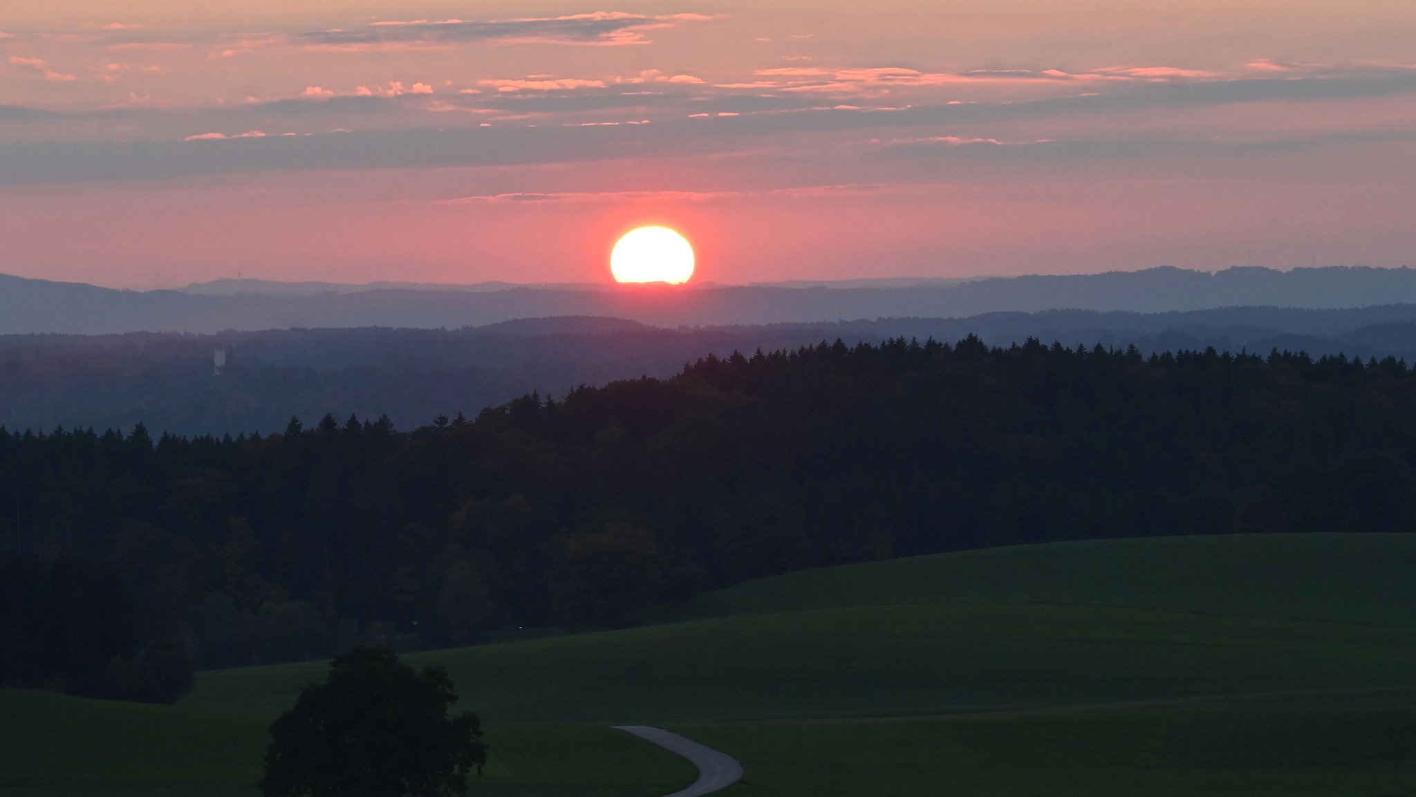 ARCHIV (12.10.2025): Die Sonne geht über den Baumwipfeln in Münsing unter.