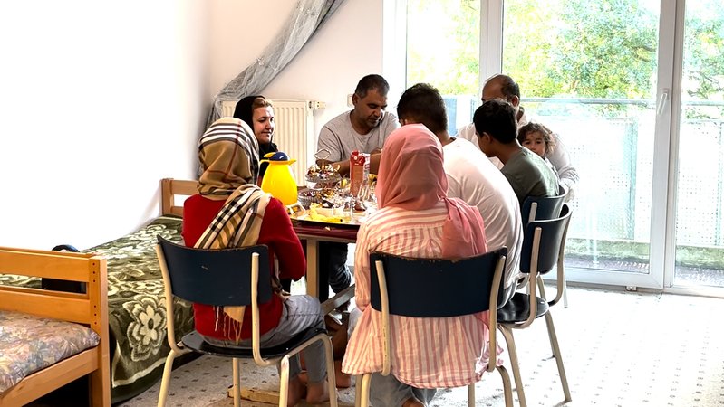 Familie Akhtari sitzt um einen Tisch und isst gemeinsam.