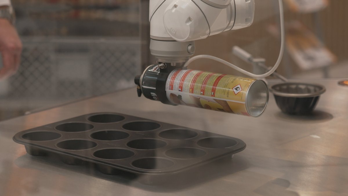 Ein Roboterarm von Boyens Backservice hält eine Sprühflasche über eine Backform