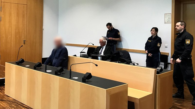 Der Angeklagte (links) im Gerichtssaal, im Hintergrund unter anderem Polizisten