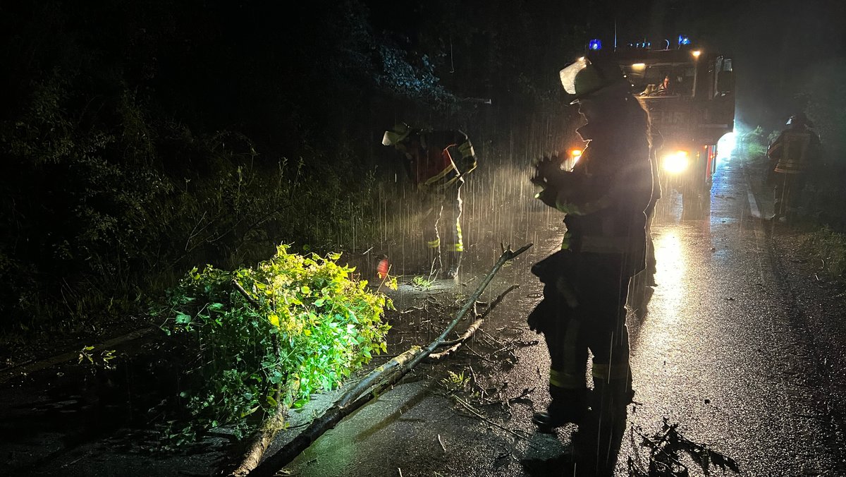 Bei strömendem Regen räumen Feuerwehrkräfte bei Berching im Landkreis Neumarkt in der Oberpfalz abgebrochene Äste von der Fahrbahn