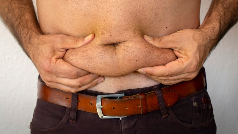 Ein Mann fasst mit beiden Händen seines Bauchs die Fettrolle | Bild: picture alliance / M.i.S. | Bernd Feil Ein Mann fasst mit beiden Händen seines Bauchs die Fettrolle