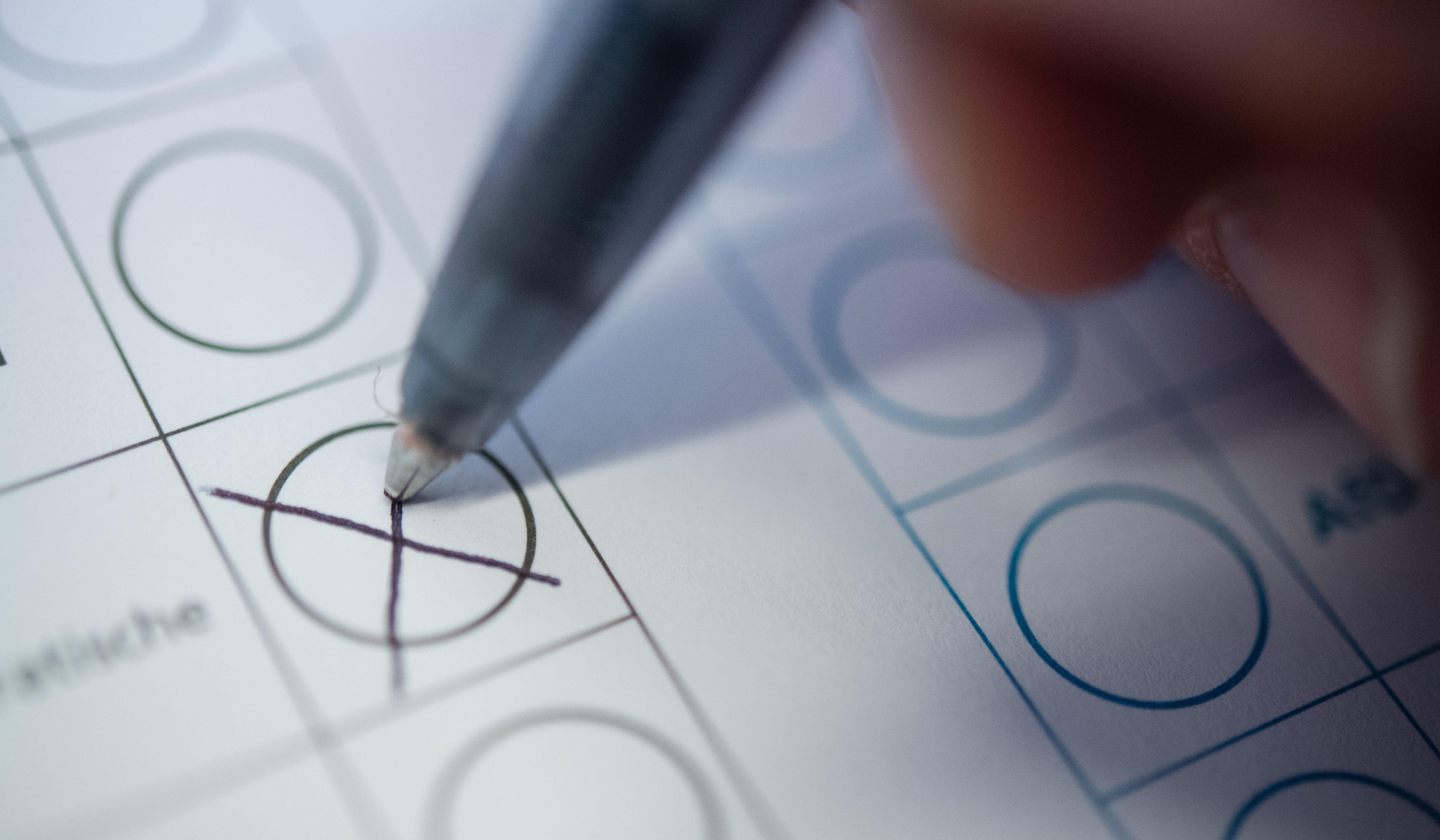 Mit einem Stift wird ein Kreuz auf einem Wahlkampfzettel gemacht. 