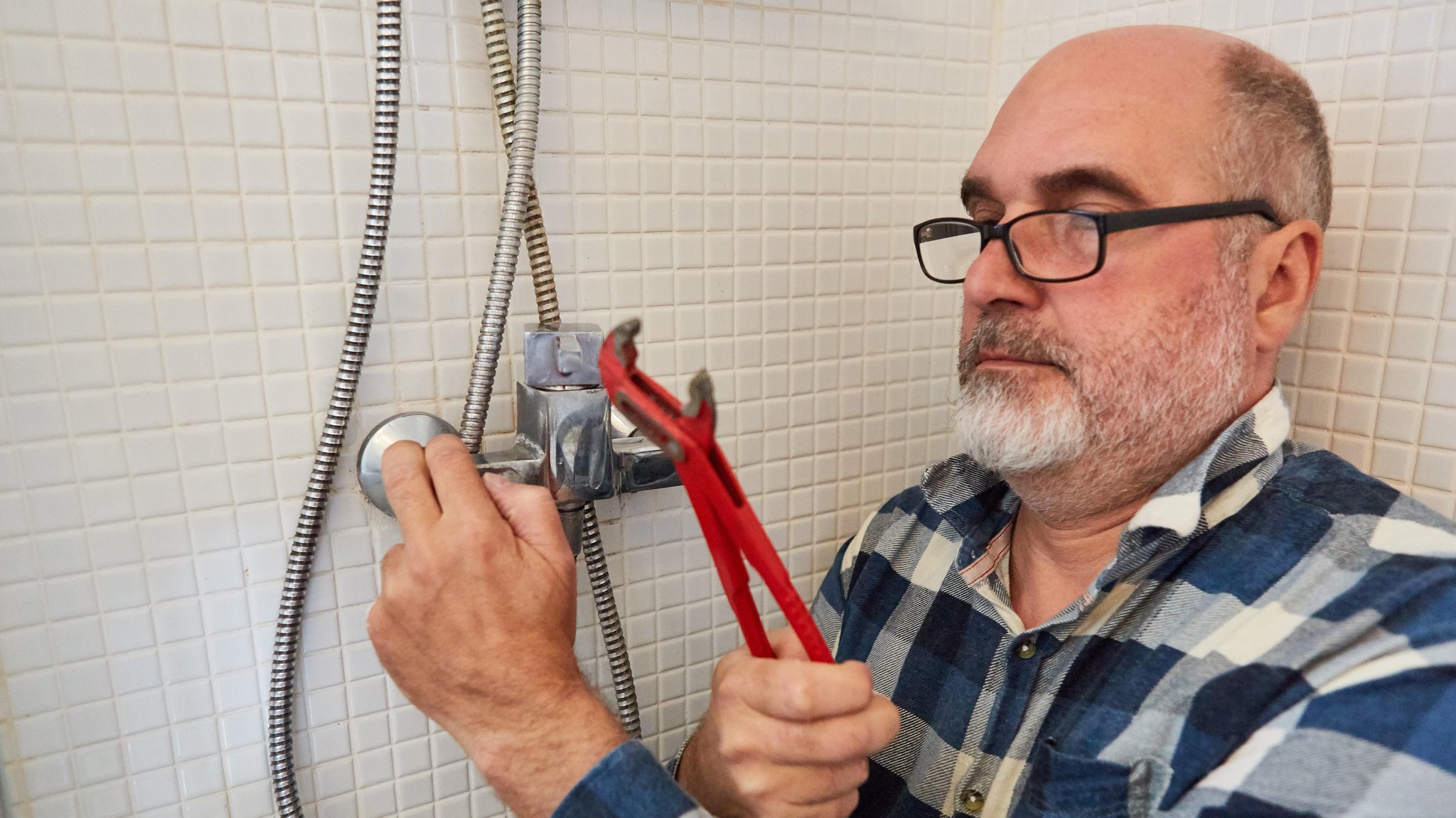 Ein Klempter montiert mit einer Rohrzange einen Brausekopf in einer Dusche. 