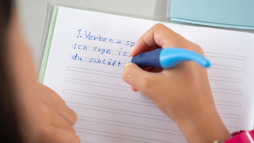 Eine Schülerin einer Grundschule soll deklinierte Verben in ihr Heft schreiben.