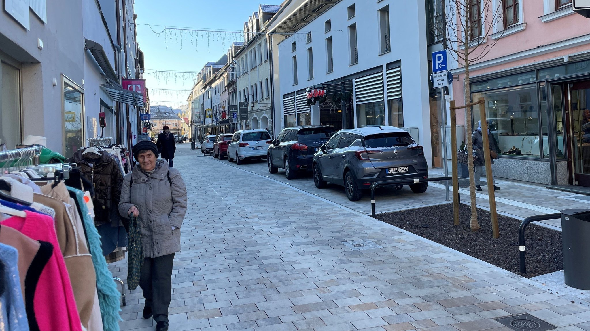 Passanten, Kleiderständer vor Geschäften und geparkte Autos in der Neuburger Innenstadt