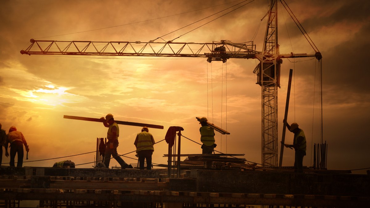 Bauarbeiter tragen Materialien auf einer Baustelle. Hinter ihnen steht ein Kran. Ihr Job kann unter Umständen sehr gefährlich sein. 74 Arbeiter verletzten sich im vergangenen Jahr tödlich auf Baustellen in Deutschland. 