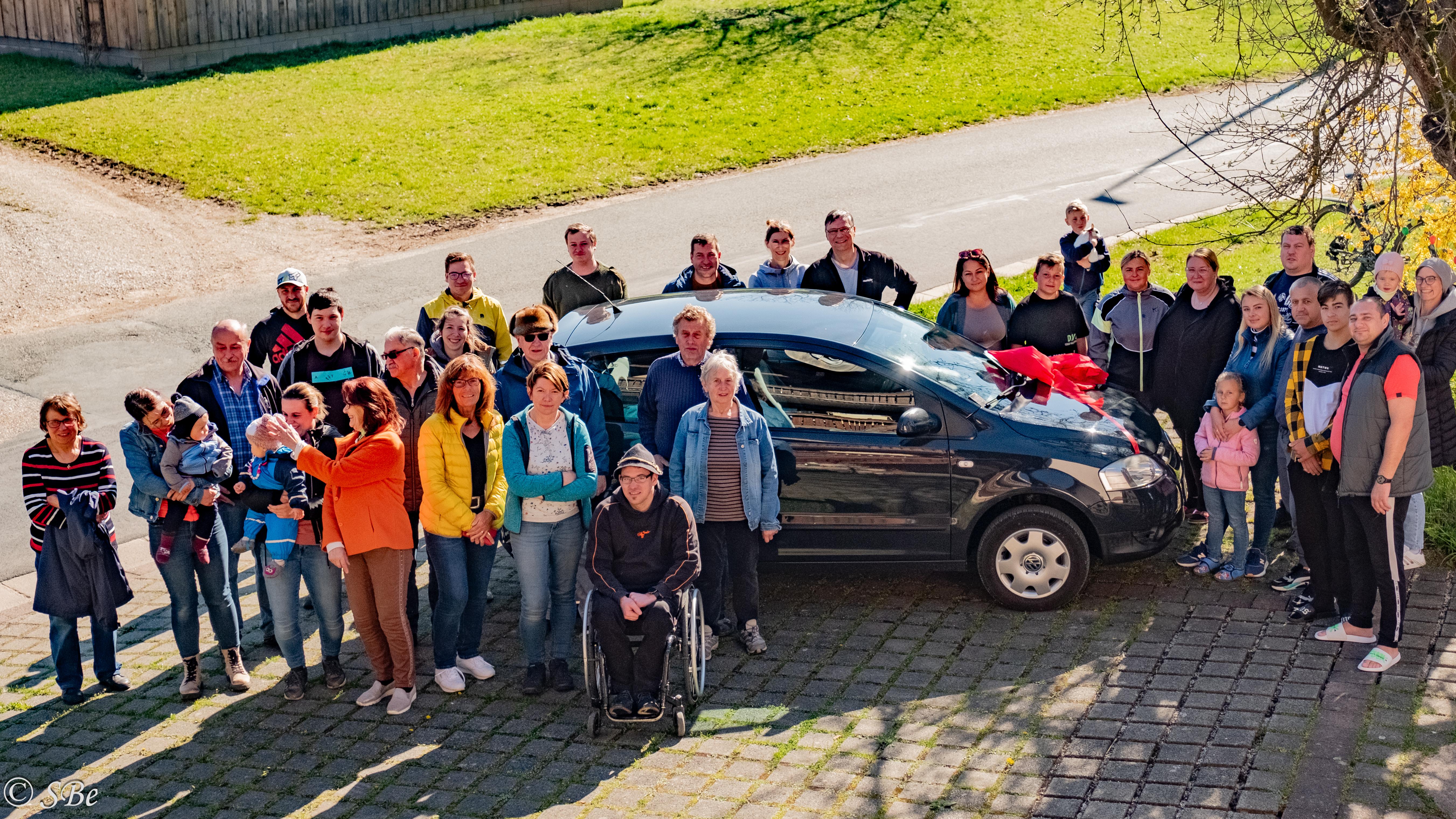 Menschen stehen in Saugendorf um ein schwarzes Auto herum.