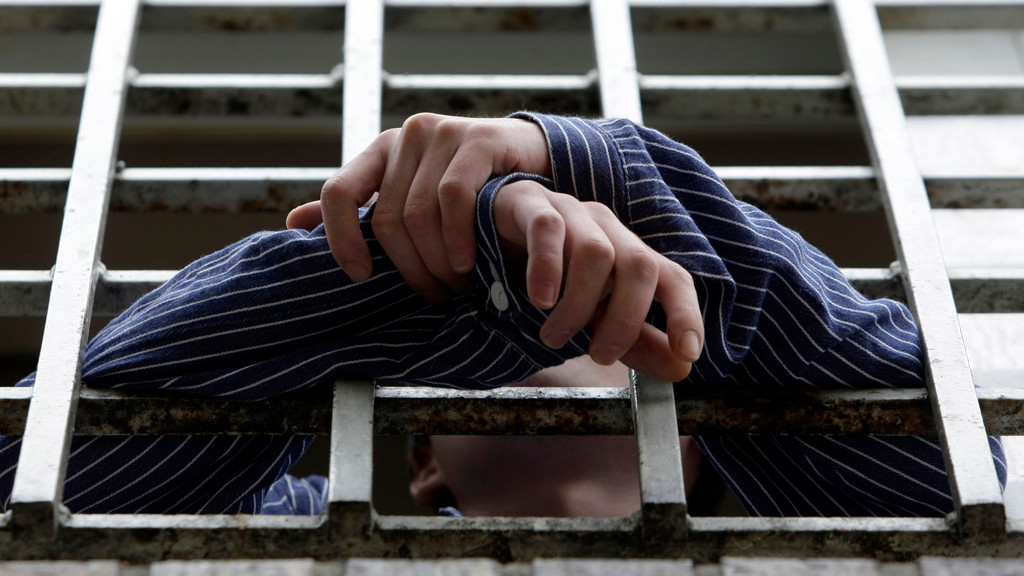 Die Hände eines Gefangenen ragen aus einem Zellenfenster.