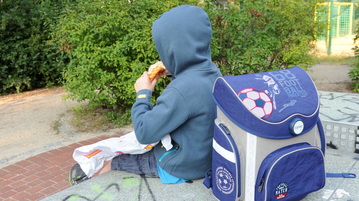 Illustration: Ein Junge sitzt mit seinem Schulranzen und Kuchen auf einer Tischtennisplatte auf einem Spielplatz.