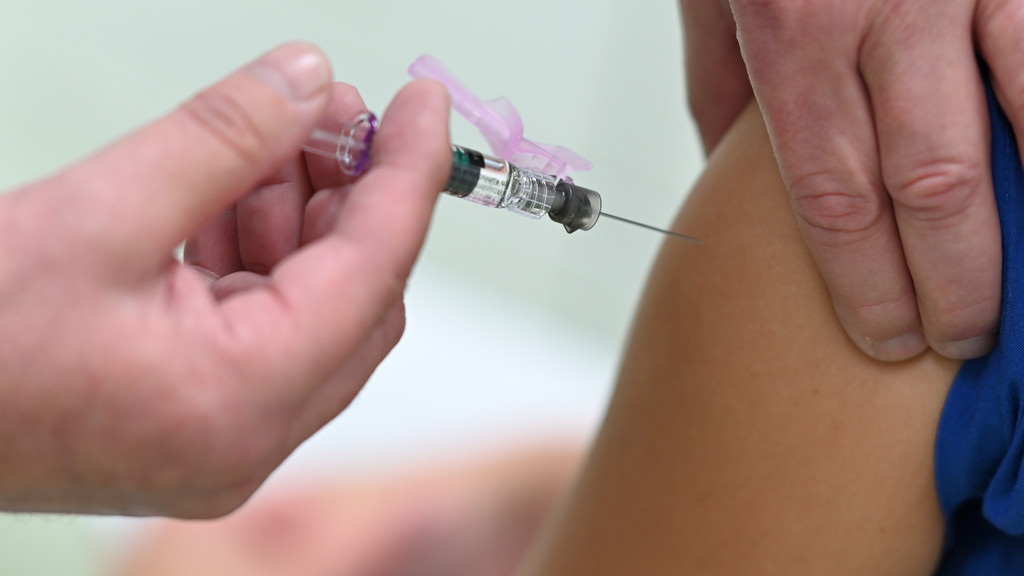 Ein Arzt impft eine Kollegin mit einem Grippeimpfstoff.