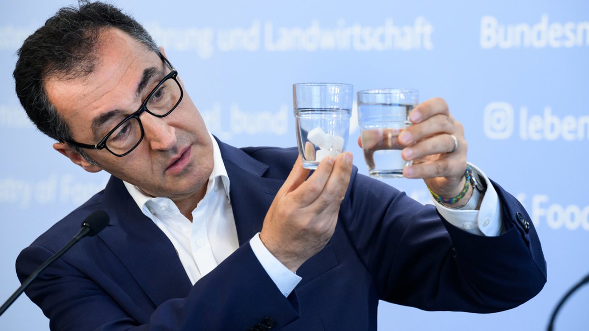 Ernährungsminister Özdemir Özdemir hält zwei Wassergläser in die Höhe, in einem befinden sich Zuckerwürfel.