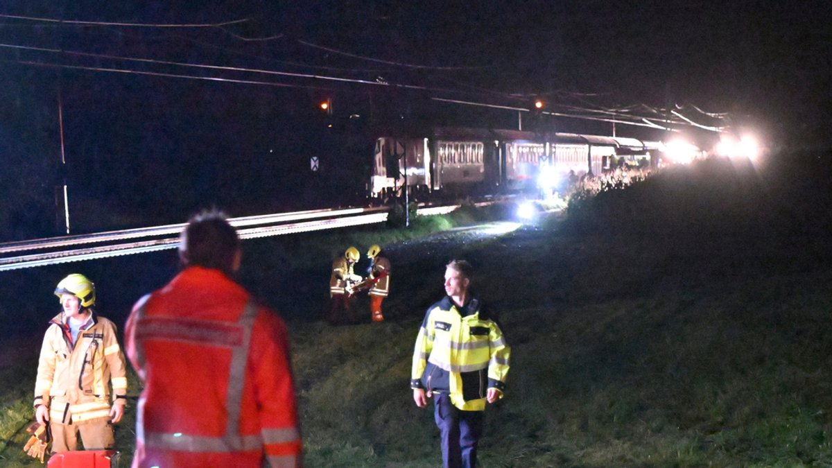 13.08.2024, Bayern, Bad Endorf: Feuerwehrleute stehen an einem Einsatzort zwischen Bad Endorf und Prien nahe dem Chiemsee, wo ein Eurocity mit einem in den Gleisbereich gestürzten Baum kollidiert und liegengeblieben ist. 