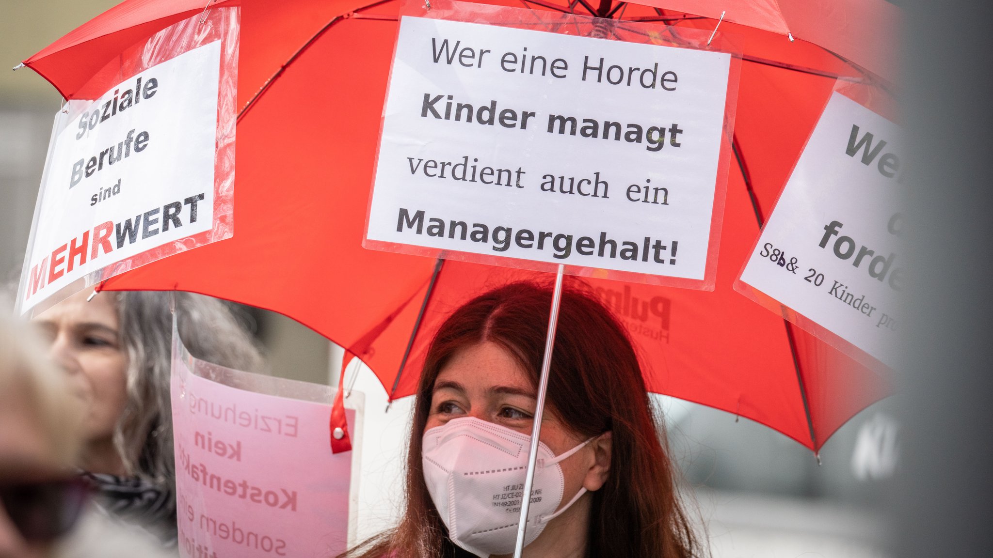 Demonstrantin trägt bei einem Protestmarsch ein Plakat mit der Aufschrift "Wer eine Horde Kinder managt verdient auch ein Managergehalt".