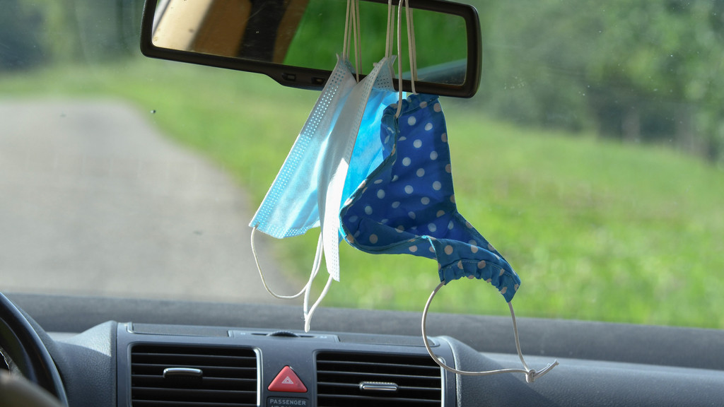 Mundschutzmasken hängen am Rückspiegel in einem Auto.