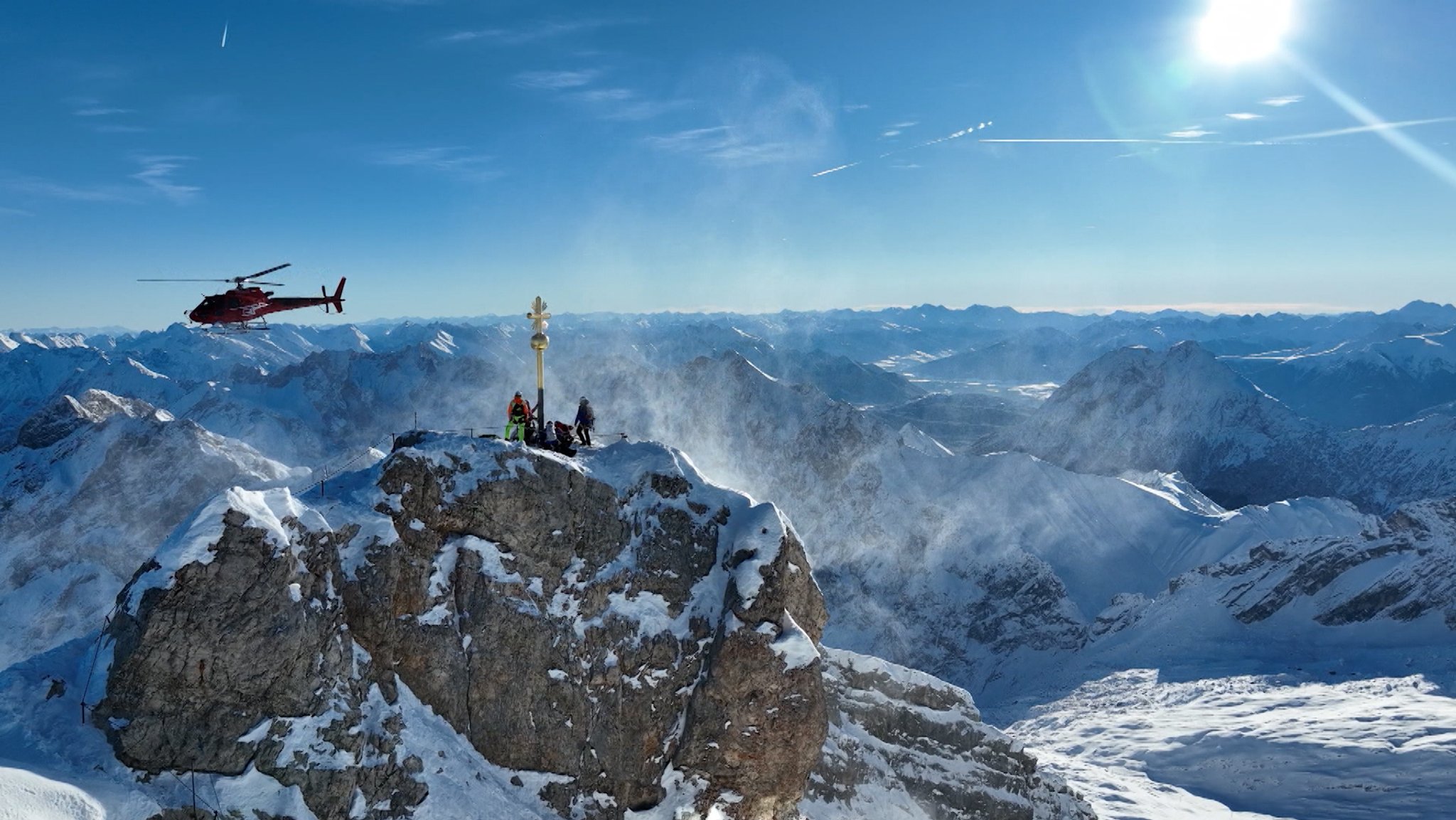 Hubschrauber fliegt über das Gipfelkreuz der Zugspitze