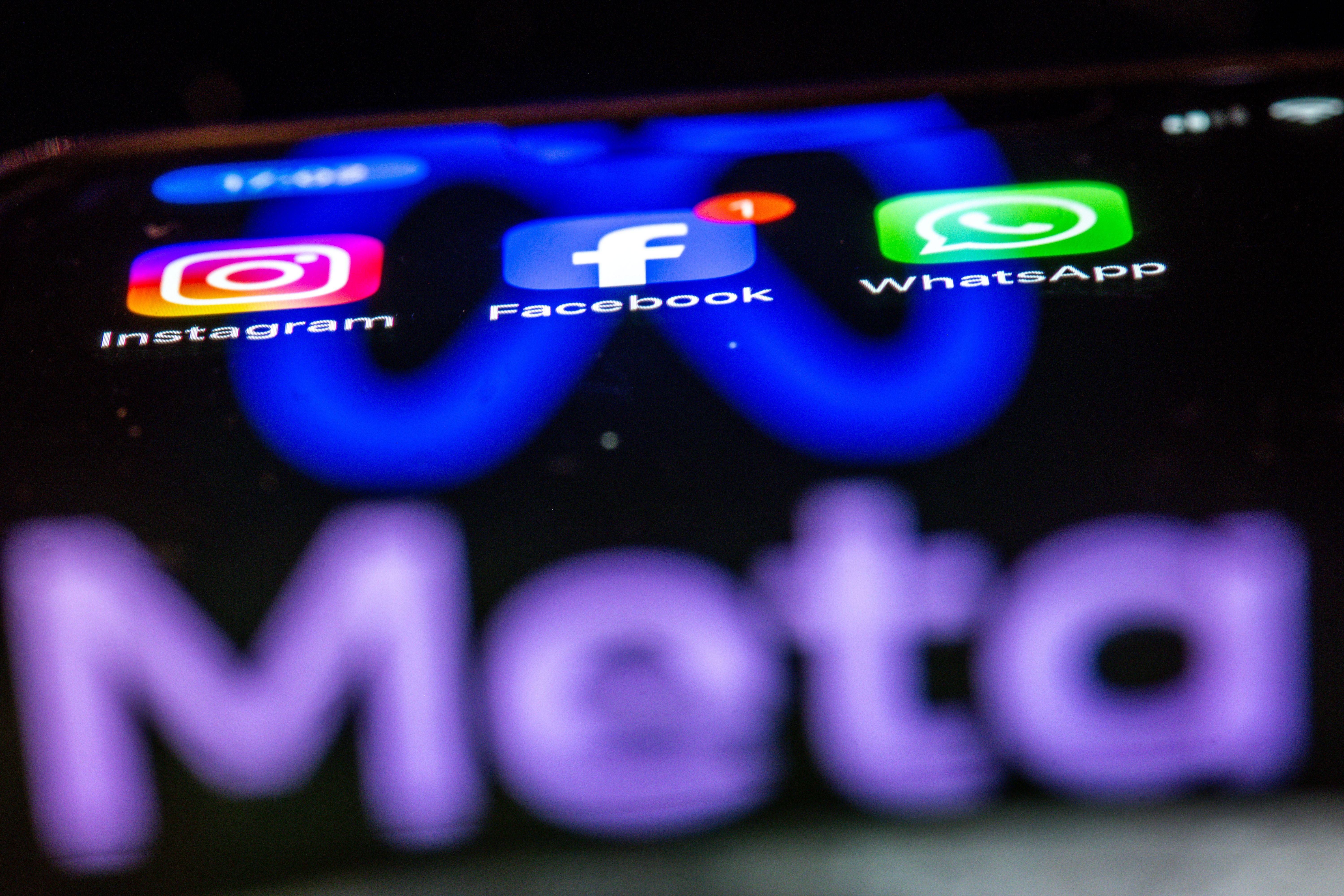 Die Apps Instagram, Facebook und WhatsApp sind auf dem Display eines Smartphones zu sehen, indem sich das Logo des Internetkonzerns Meta spiegelt.