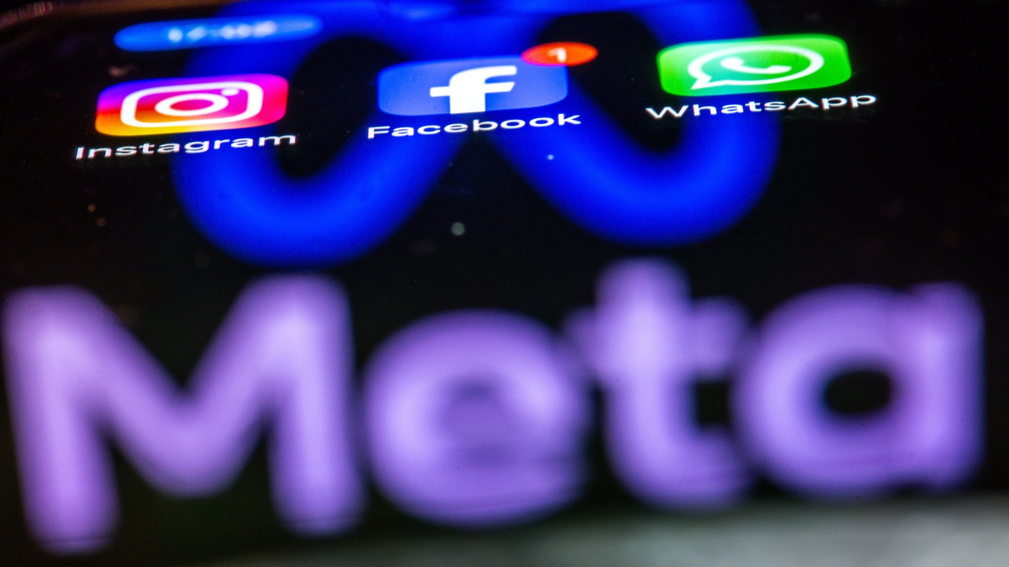Die Apps Instagram, Facebook und WhatsApp sind auf dem Display eines Smartphones zu sehen, indem sich das Logo des Internetkonzerns Meta spiegelt.