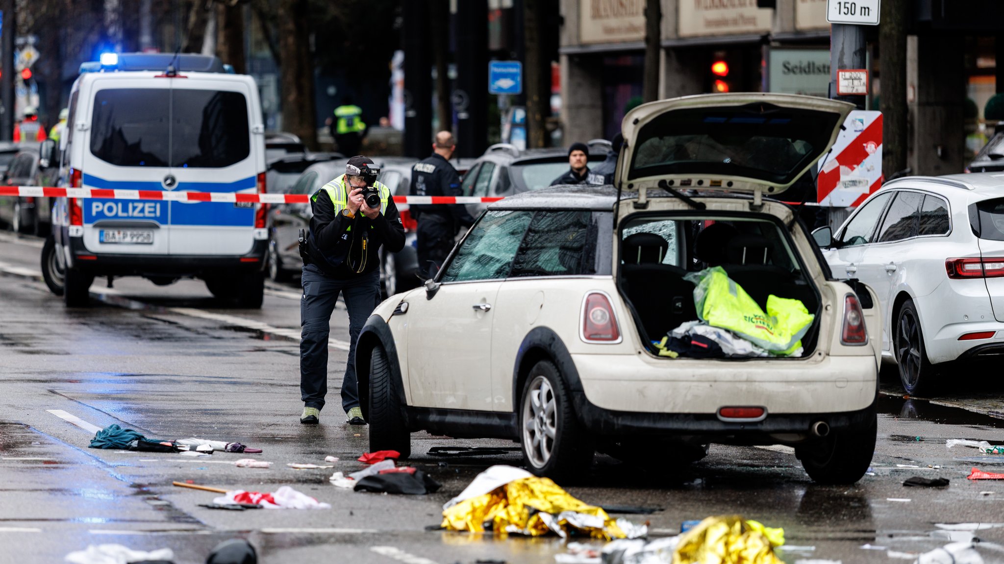 Ein Polizist fotografiert ein Auto am Einsatzort. In der Münchner Maxvorstadt ist ein Fahrzeug in eine Menschengruppe gefahren.