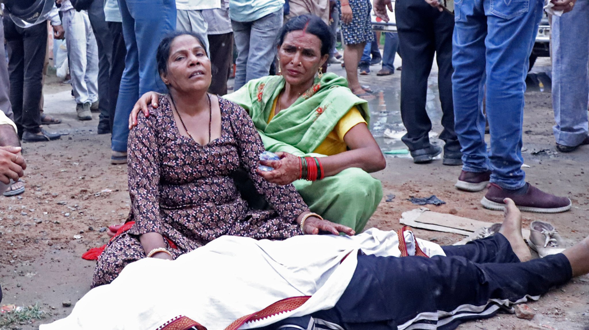 02.07.2024, Indien, Hathras: Frauen trauern neben der Leiche eines Verwandten vor dem Sikandrarao-Krankenhaus, etwa 350 Kilometer (217 Meilen) südwestlich von Luckno. 