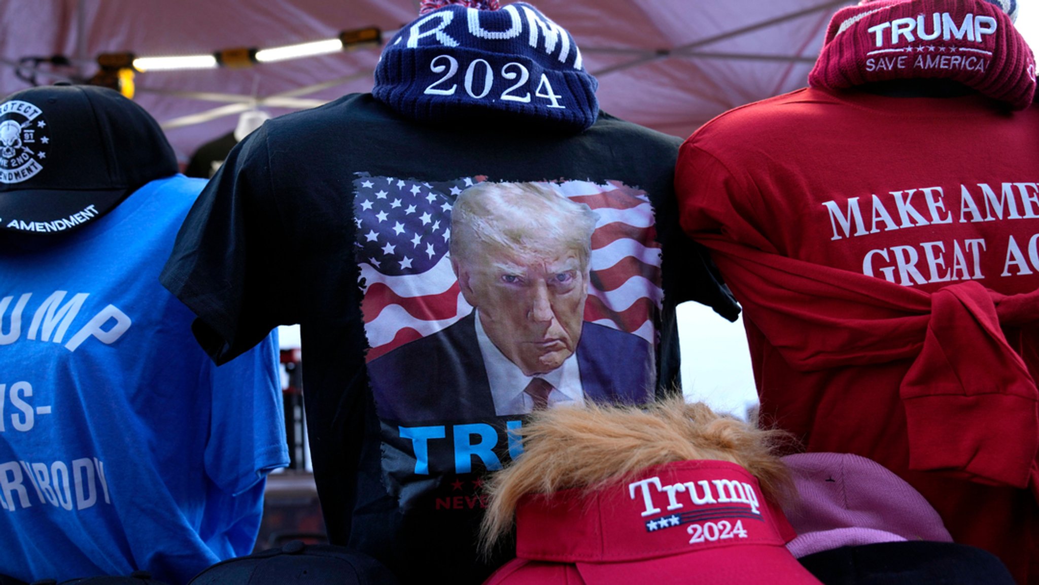 T-Shirts, Sweatshirts und Mützen mit dem Bild und dem Namen des ehemaligen US-Präsidenten Trump, den Schriftzügen "Make America Great Again" (Mach Amerika wieder großartig), "Trump Save America" (Trump rette Amerika) und "Jesus is my Savior" (Jesus ist mein Retter) werden an einem Verkaufsstand angeboten vor einer Commit-to-Caucus-Kundgebung in Coralville, Iowa.