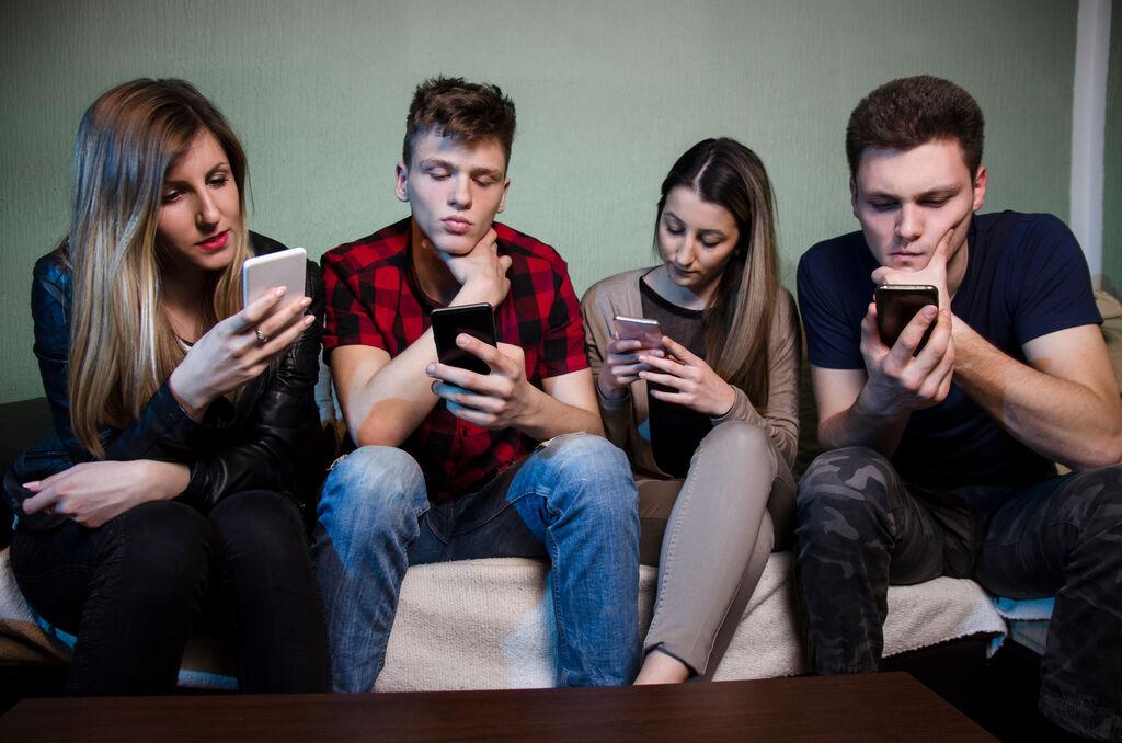 Vier junge Erwachsene schauen in ihre Smartphones.