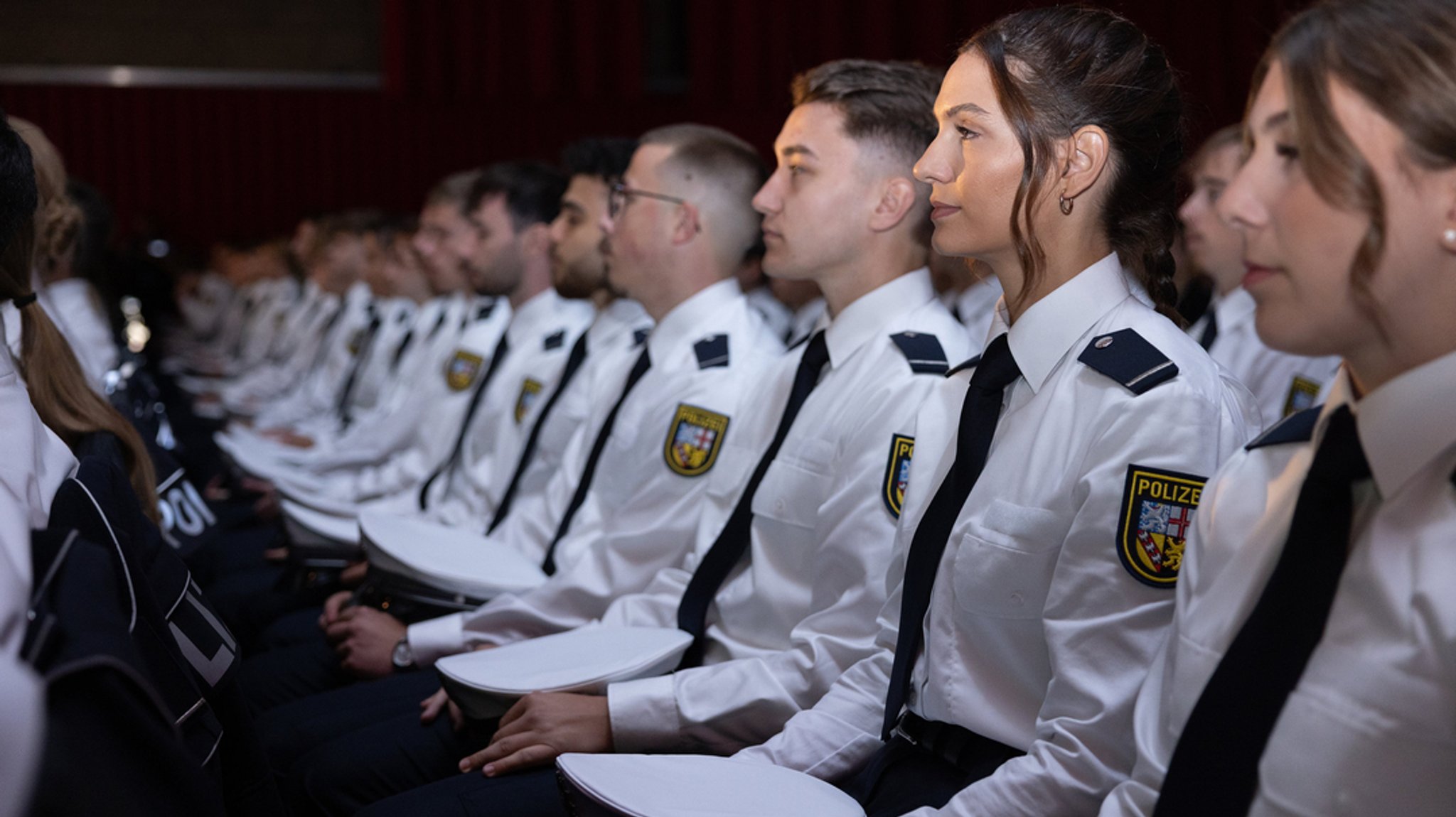 Angehende Kommissaranwärterinnen und -anwärter sitzen bei ihrer Vereidigung im Saal.