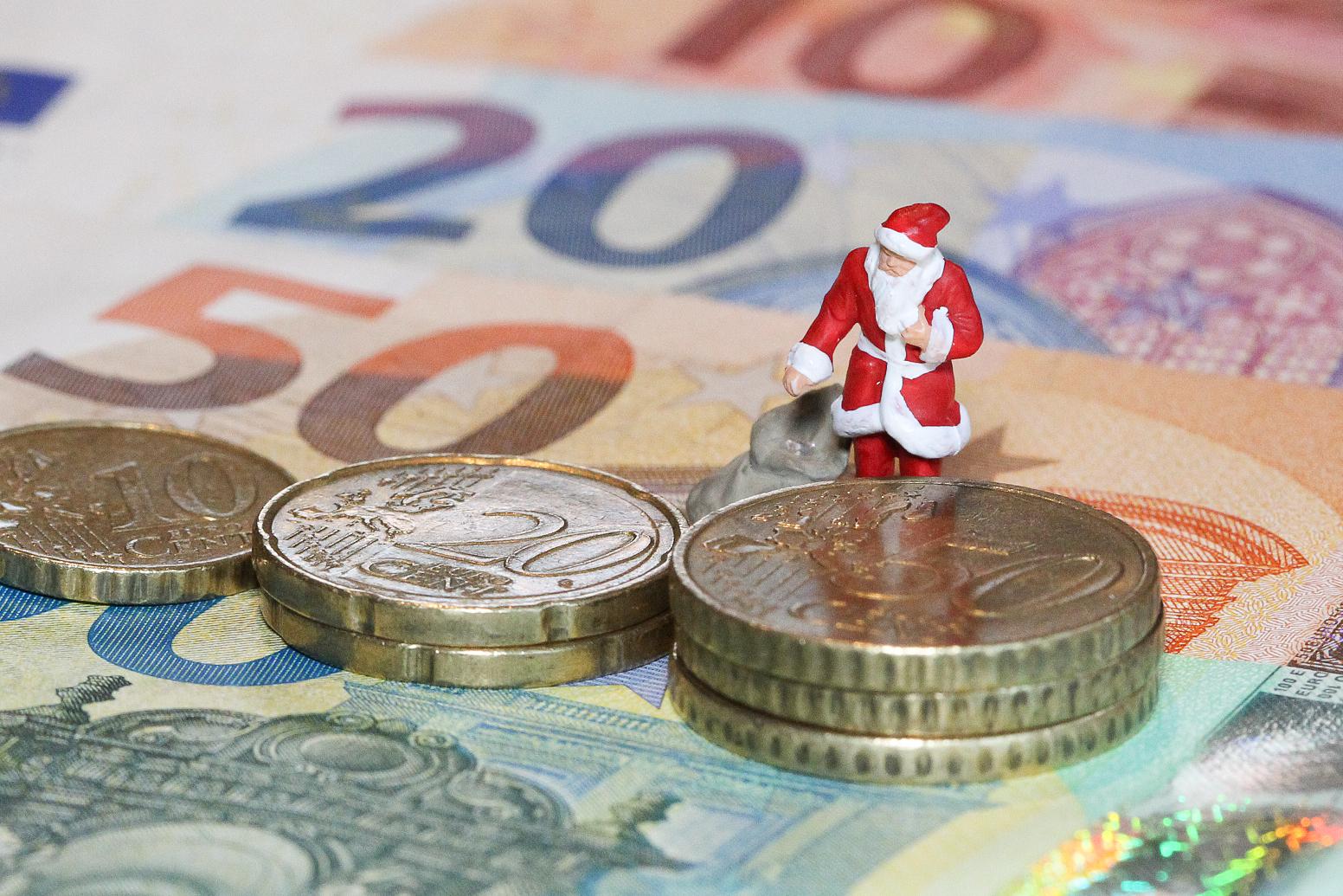 Weihnachtsmann in Miniatur mit Gabensack steht auf Banknoten, Geldscheinen und Münzen, Euromünzen, Euros