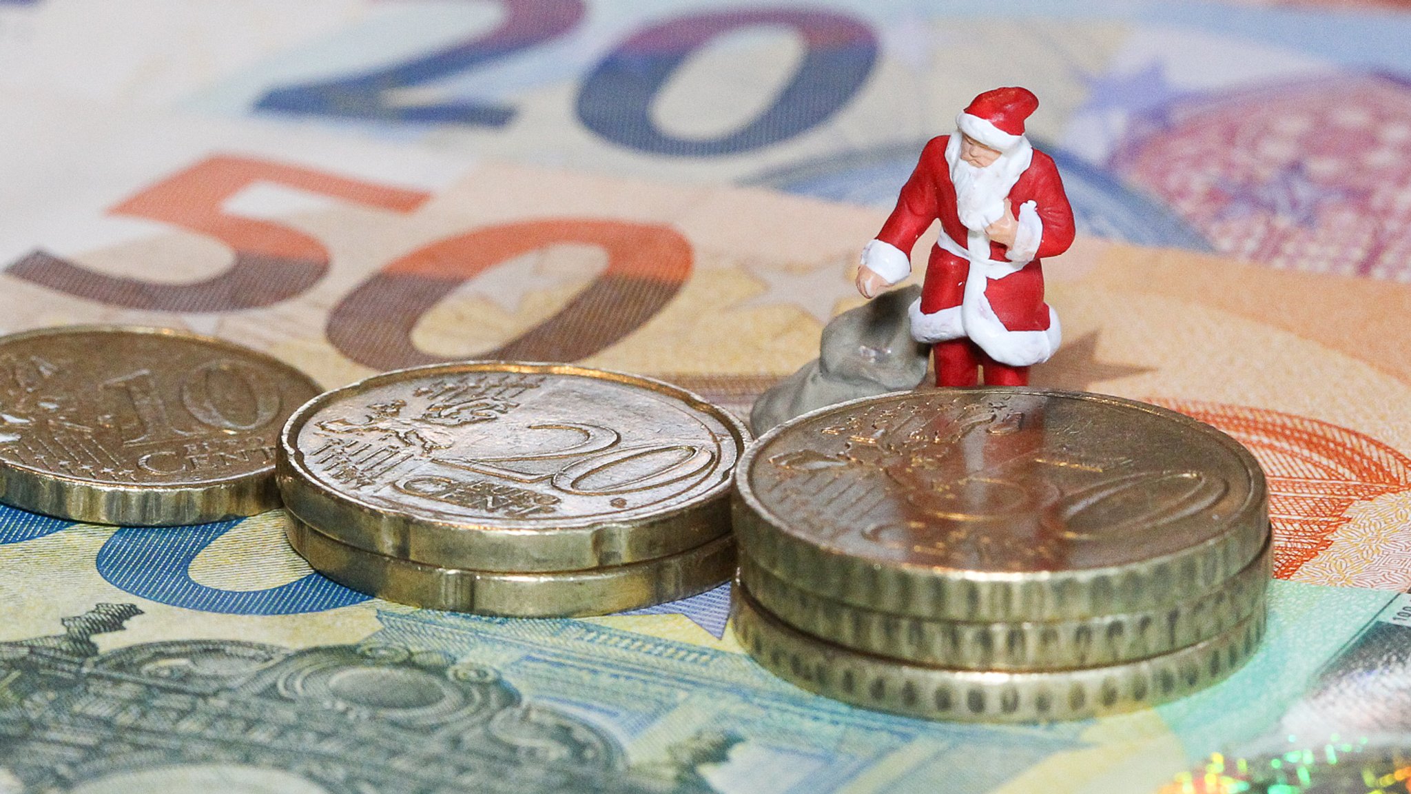 Weihnachtsmann in Miniatur mit Gabensack steht auf Banknoten, Geldscheinen und Münzen, Euromünzen, Euros