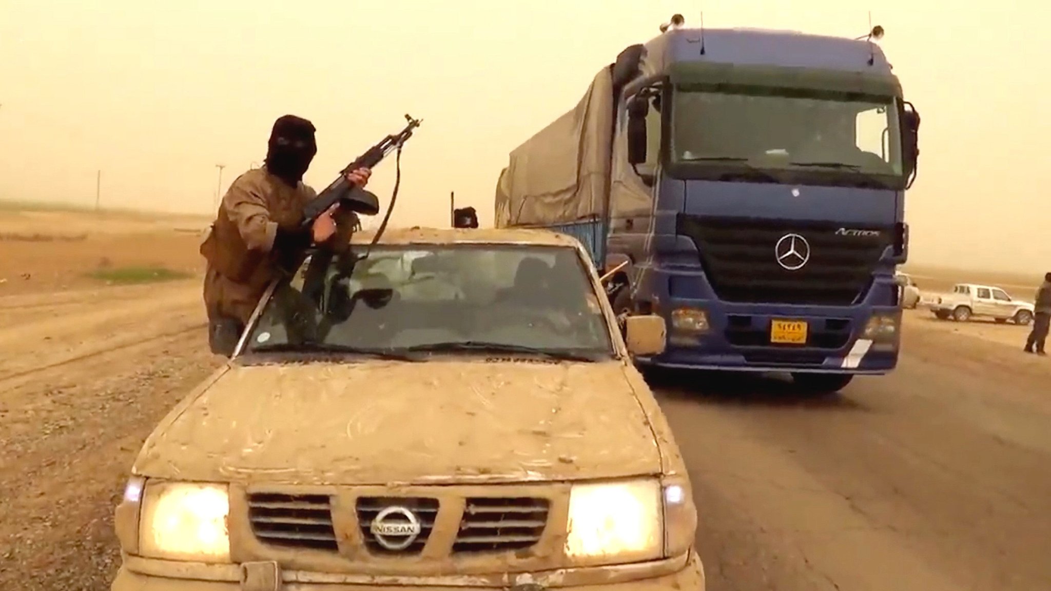(Archivbild): IS-PropagandaL Ein Mann mit einer Langwaffe lehnt sich aus einem staubigen Auto heraus, daneben steht ein großer Lkw. | Bild: pa/dpa/ZUMAPRESS.com | Handout (Archivbild): IS-PropagandaL Ein Mann mit einer Langwaffe lehnt sich aus einem staubigen Auto heraus, daneben steht ein großer Lkw.