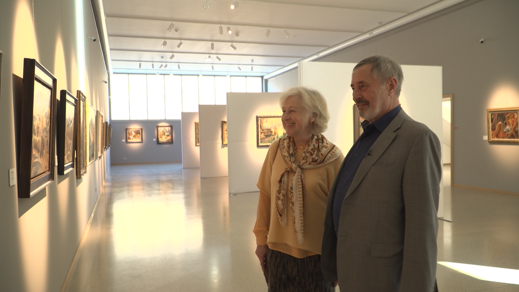 Zwei Menschen blicken in einer Galerie lächelnd auf ein Gemälde.
